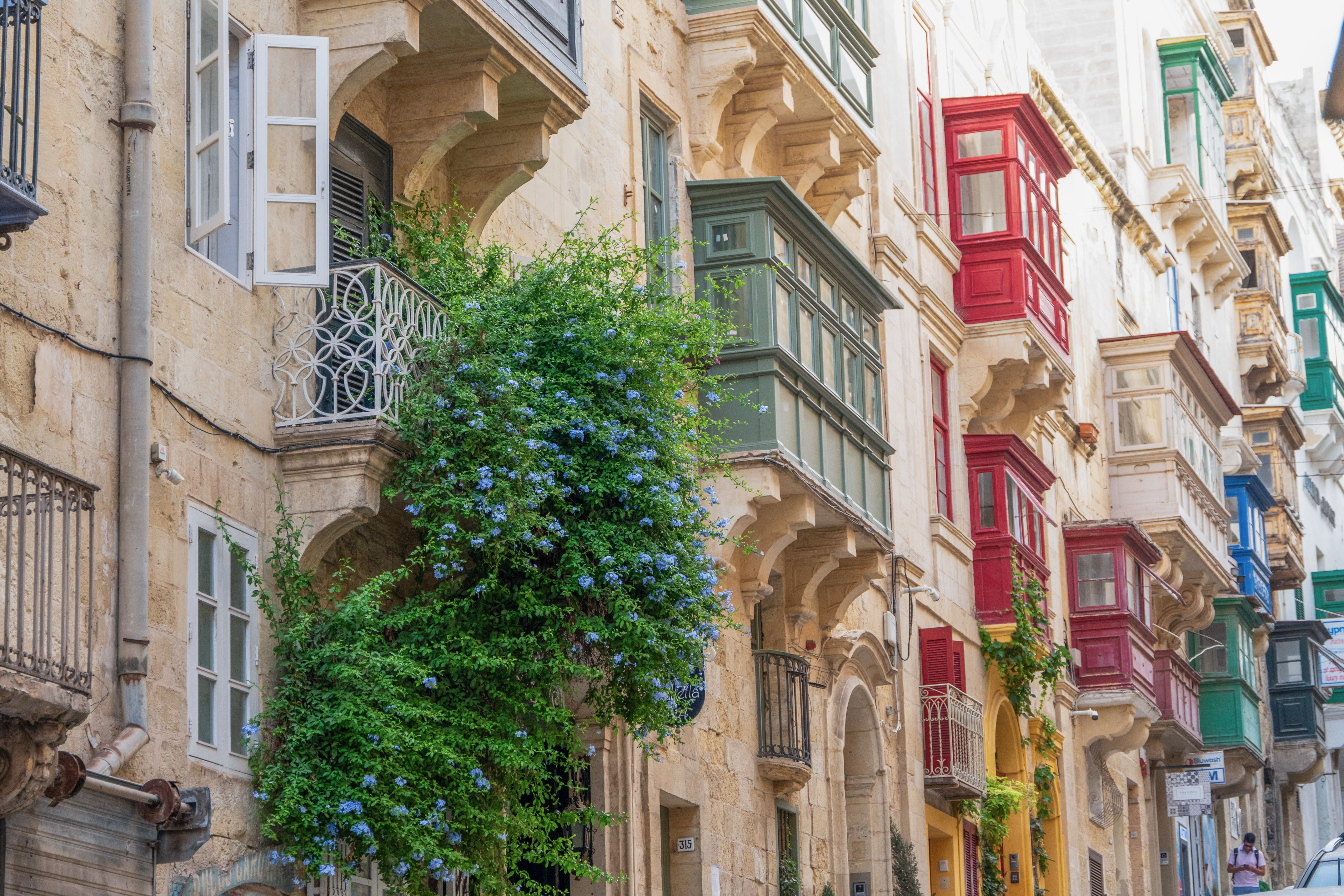 Traditional colorful Maltese balconies on a Valletta street with blue flowers.