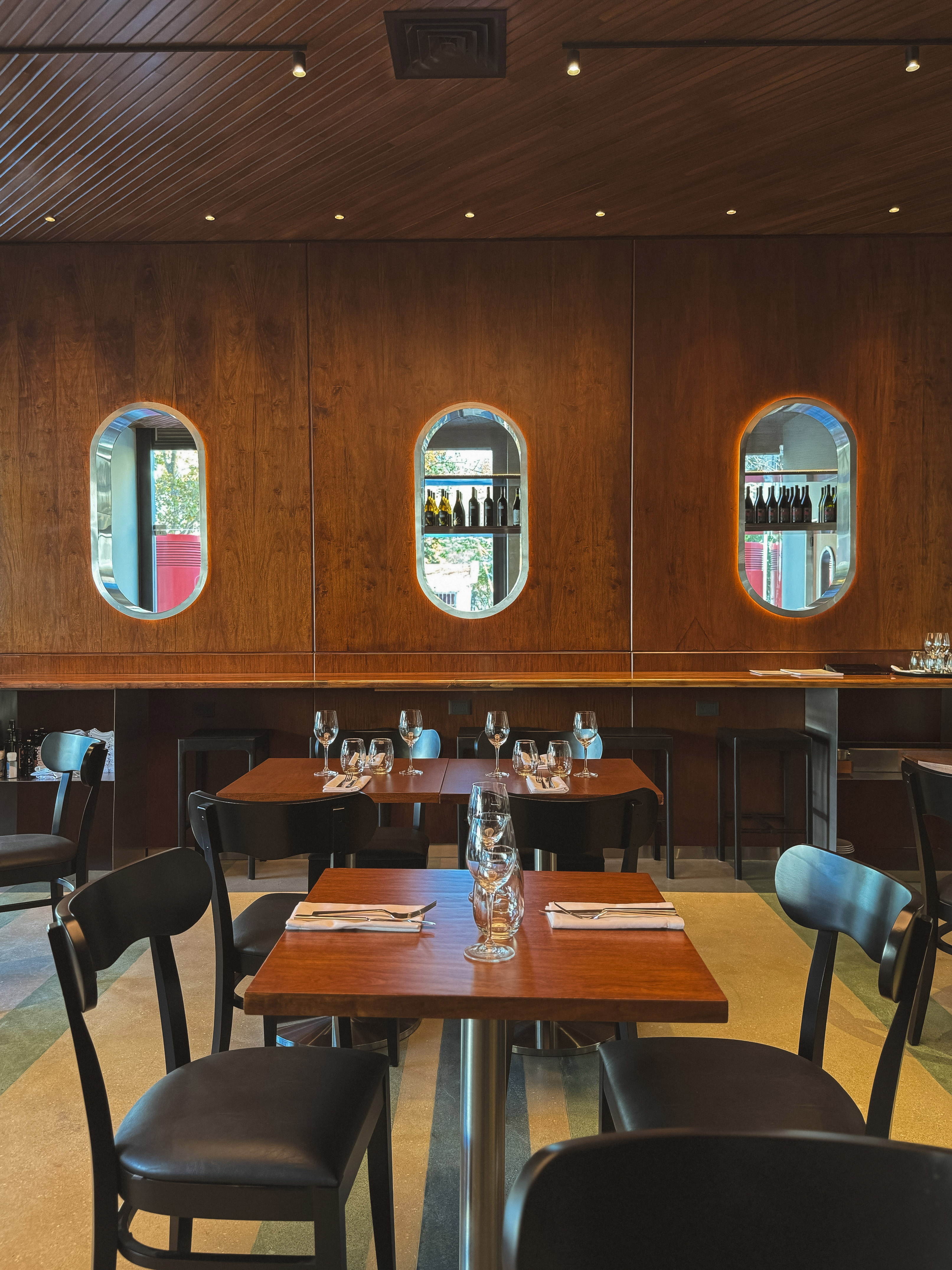 Wooden-paneled restaurant dining room with set tables and oval wine displays.