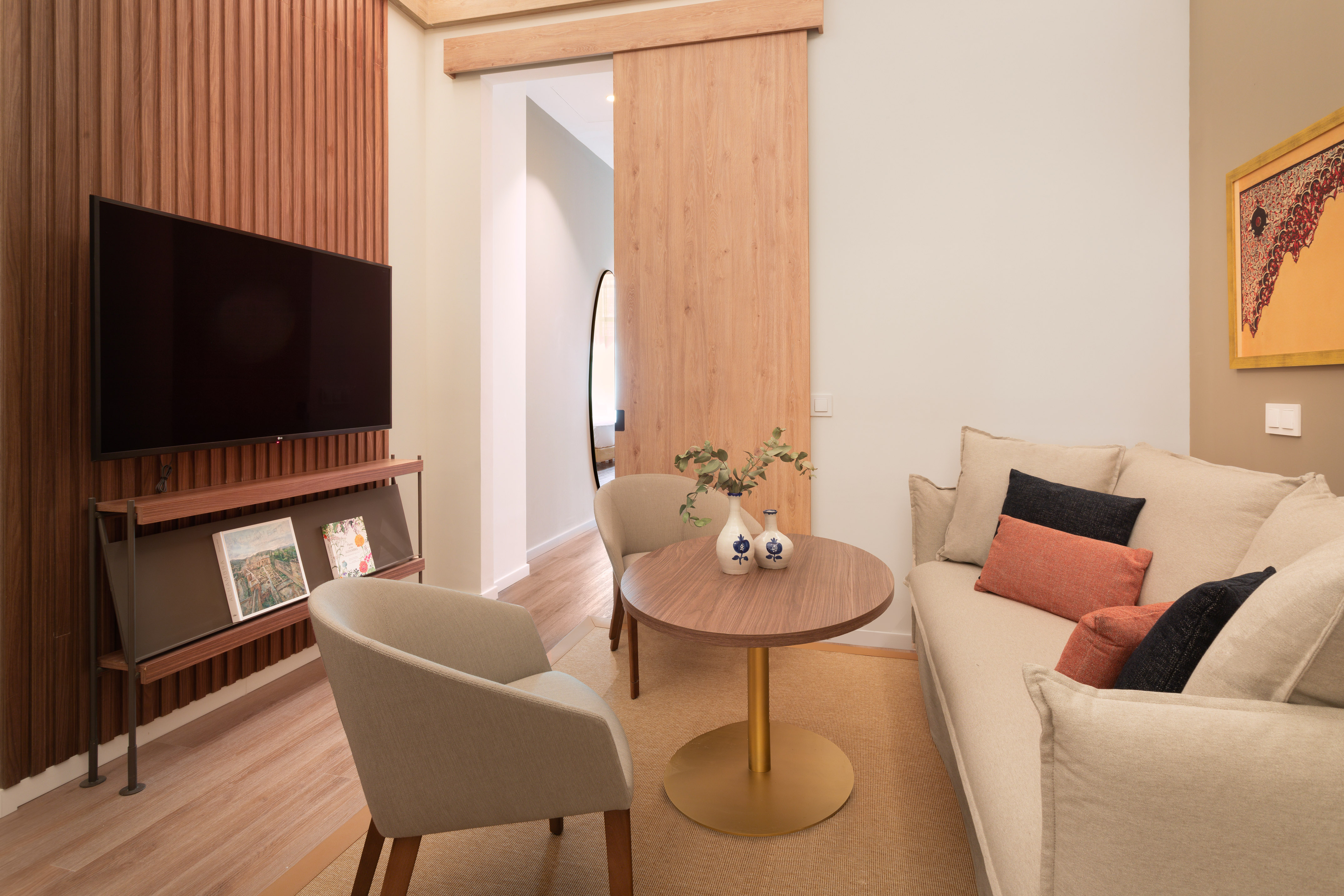 Modern living room with sofa, armchairs, TV, wood paneling, and sliding door.