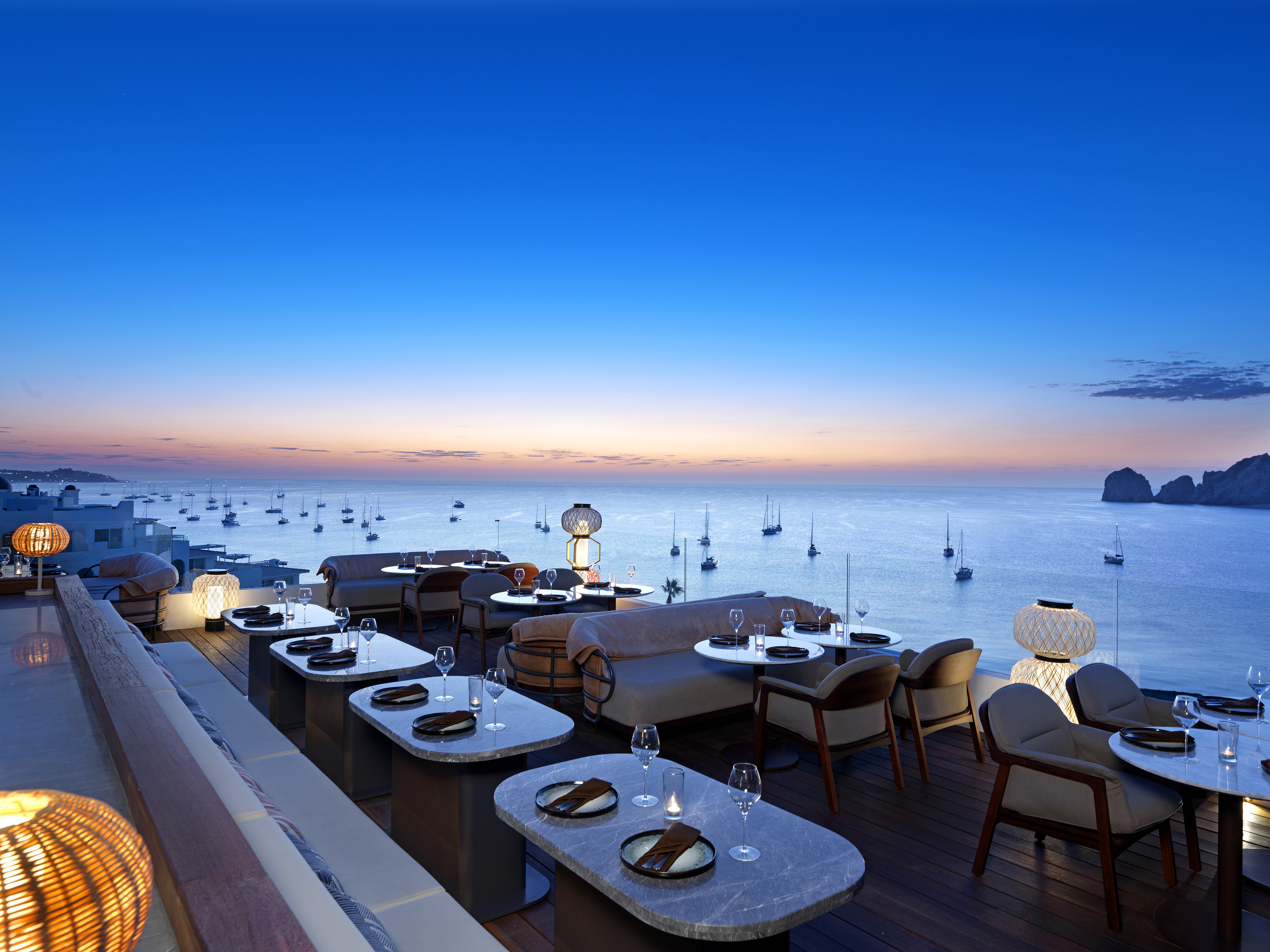 Luxury rooftop restaurant with ocean view, boats, and twilight sky.