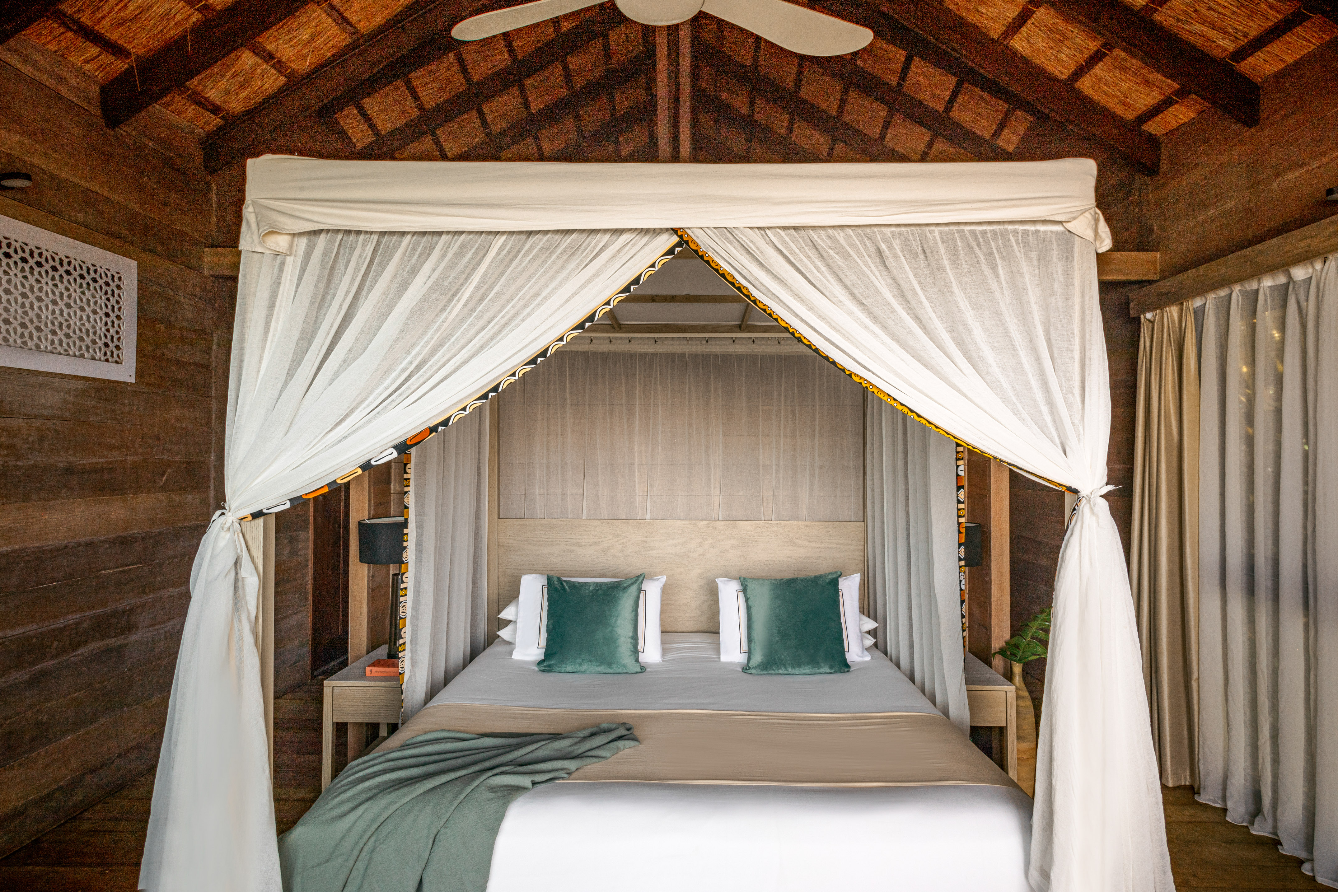 Rustic wooden bedroom with canopy bed, teal pillows, and thatched ceiling.