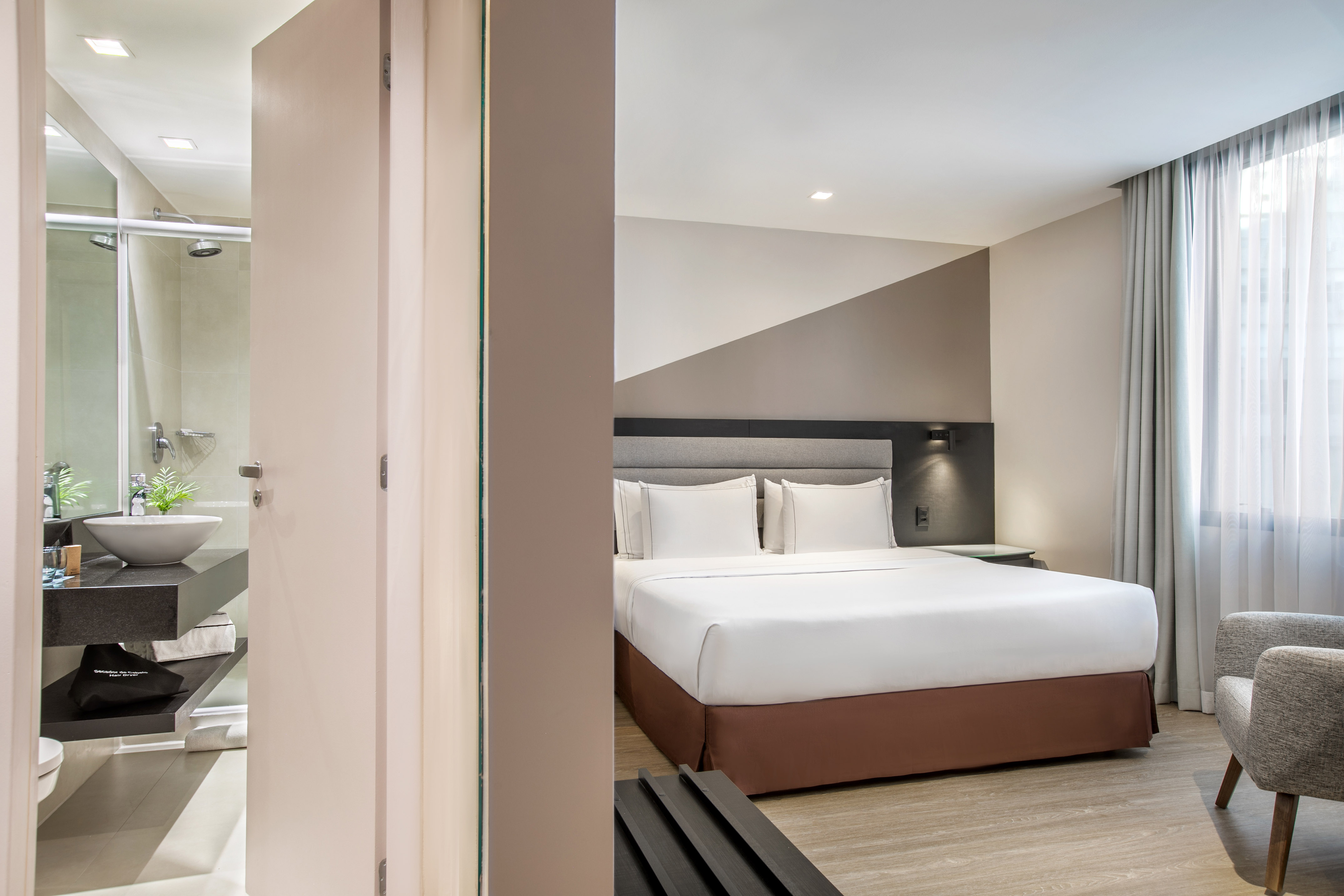 Modern hotel bedroom with a king-size bed and an adjoining bathroom with a vessel sink.