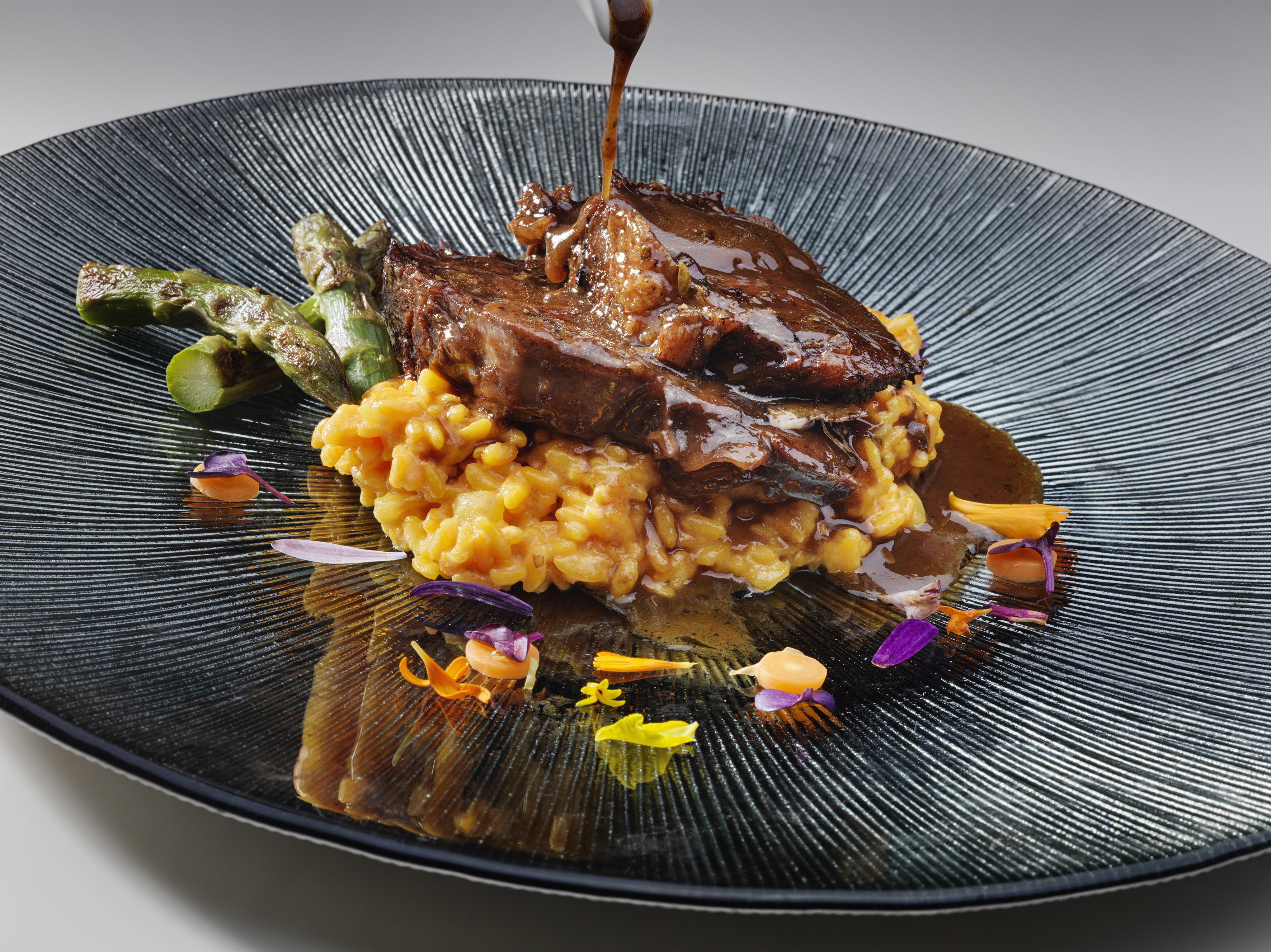 Braised beef short ribs with saffron risotto, asparagus, and rich gravy.