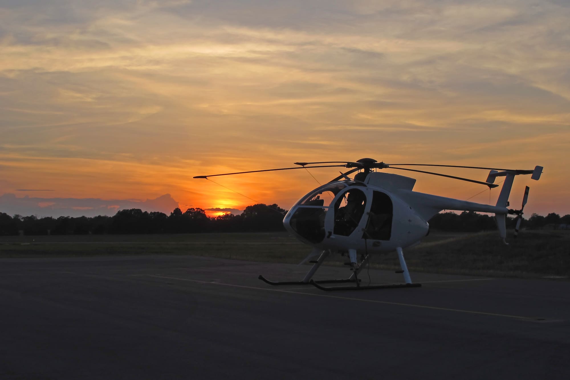 Helicóptero blanco en pista al atardecer, cielo naranja y amarillo.