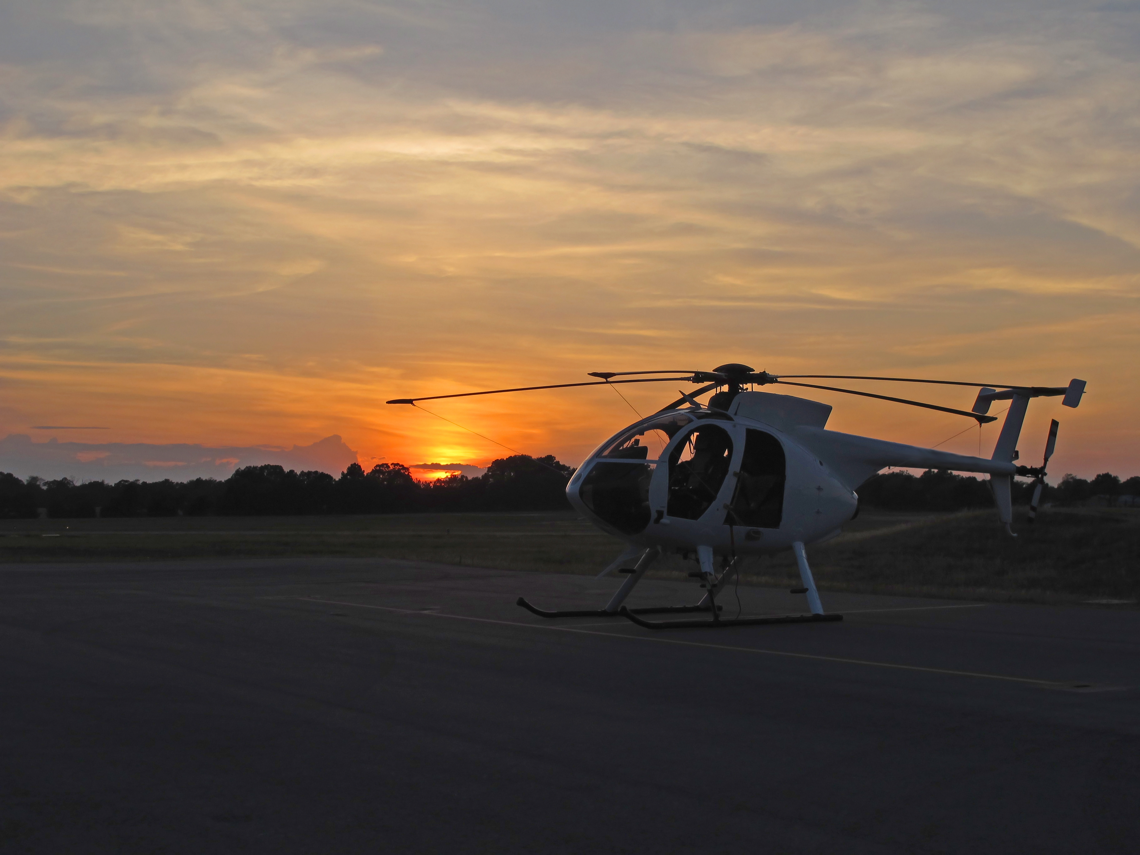 Helicóptero blanco en pista al atardecer, cielo naranja y amarillo.
