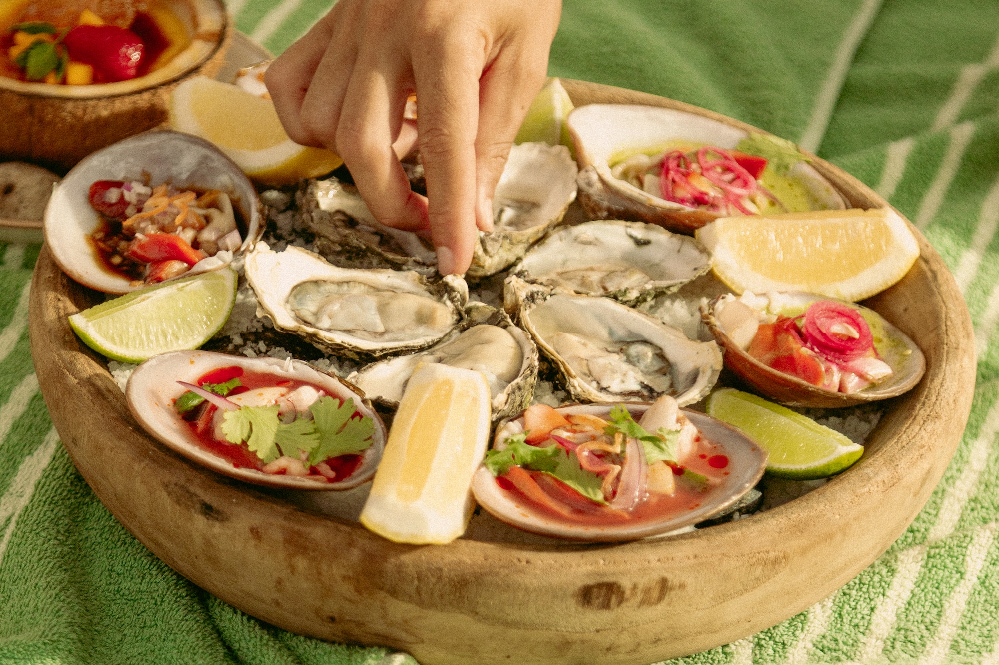 Mano cogiendo ostra de bandeja de mariscos y ceviche con limones.