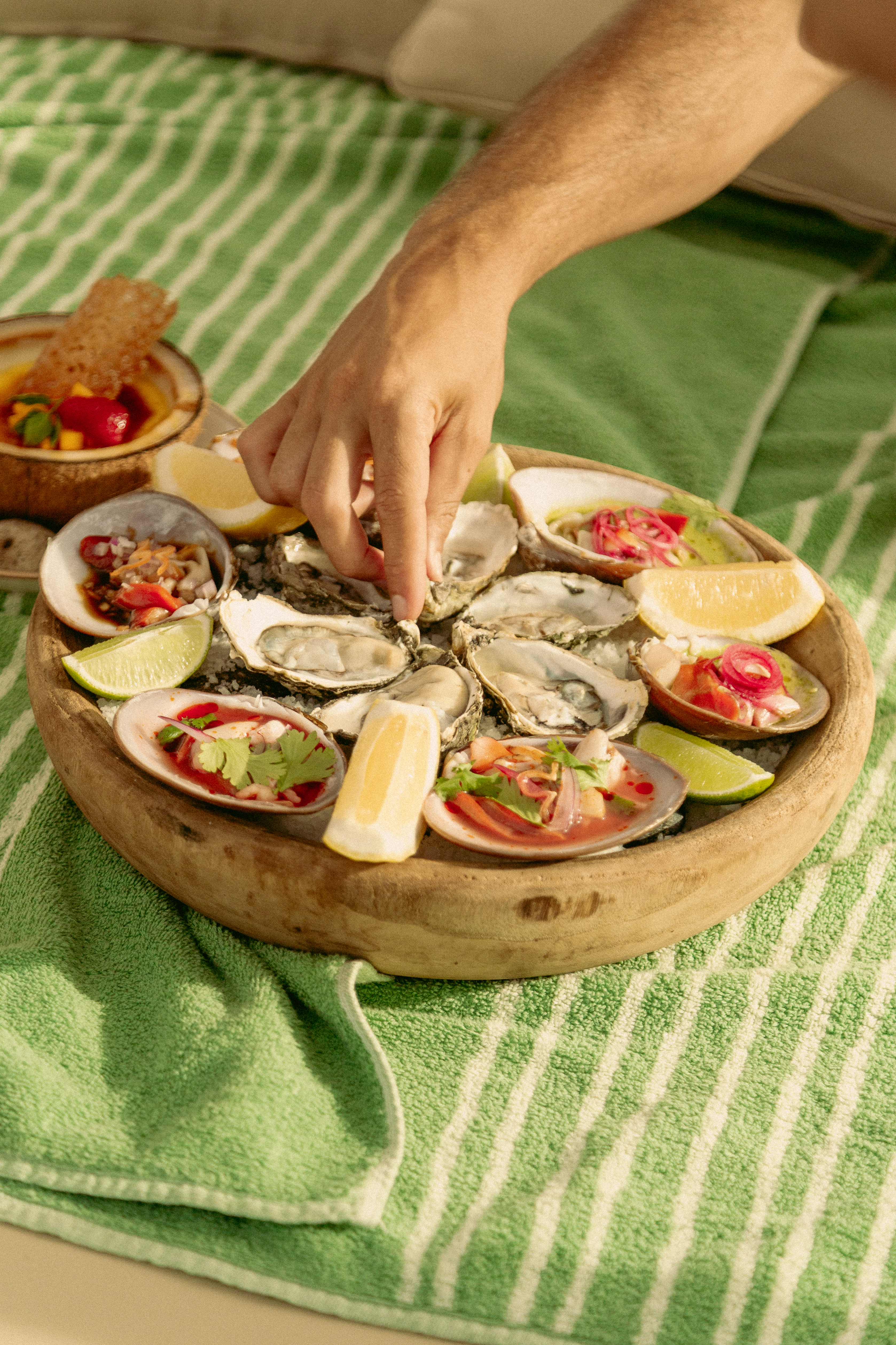 Mano cogiendo ostra de bandeja de mariscos y ceviche con limones.