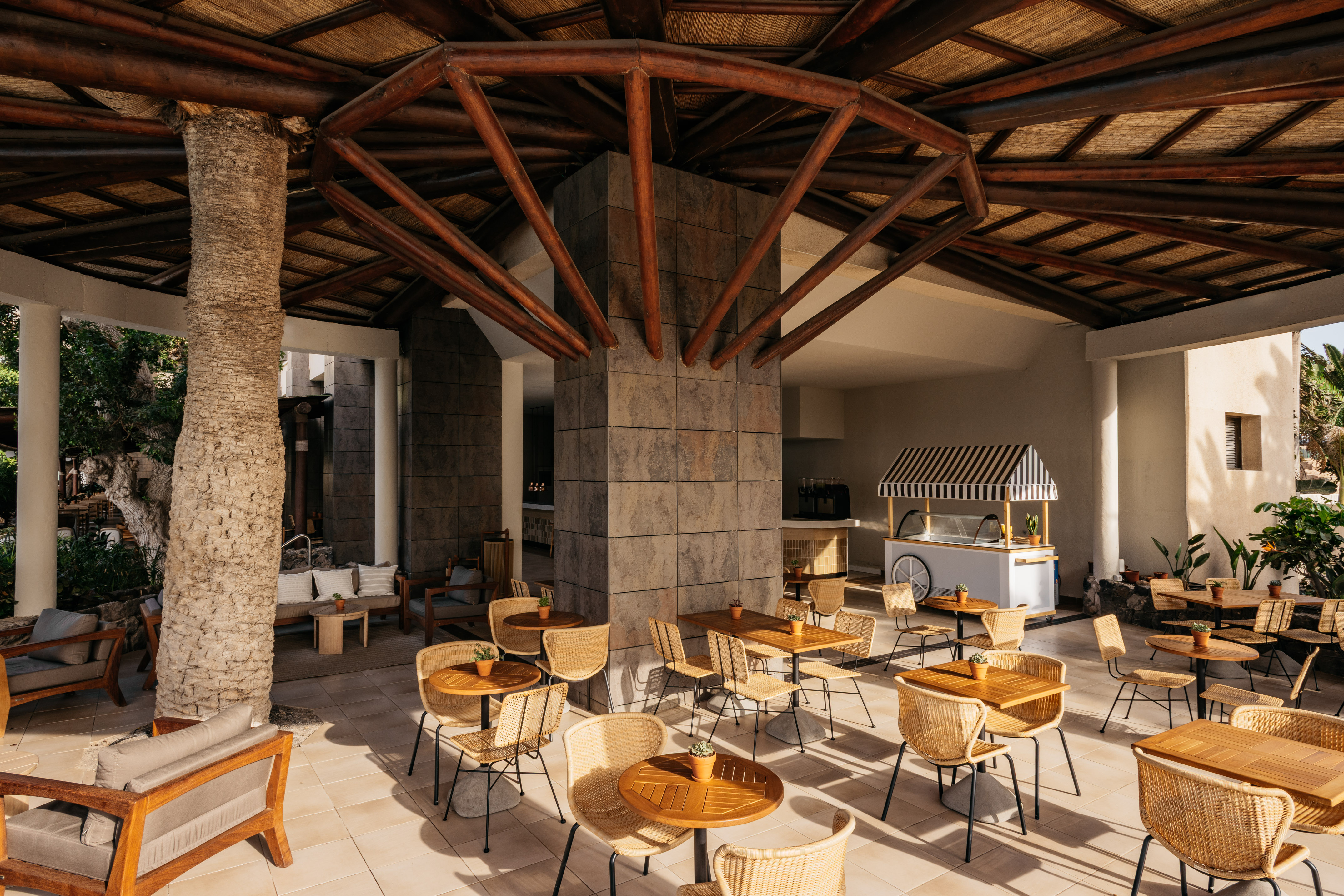 Outdoor resort cafe patio with wicker chairs, wooden tables, and thatched roof.