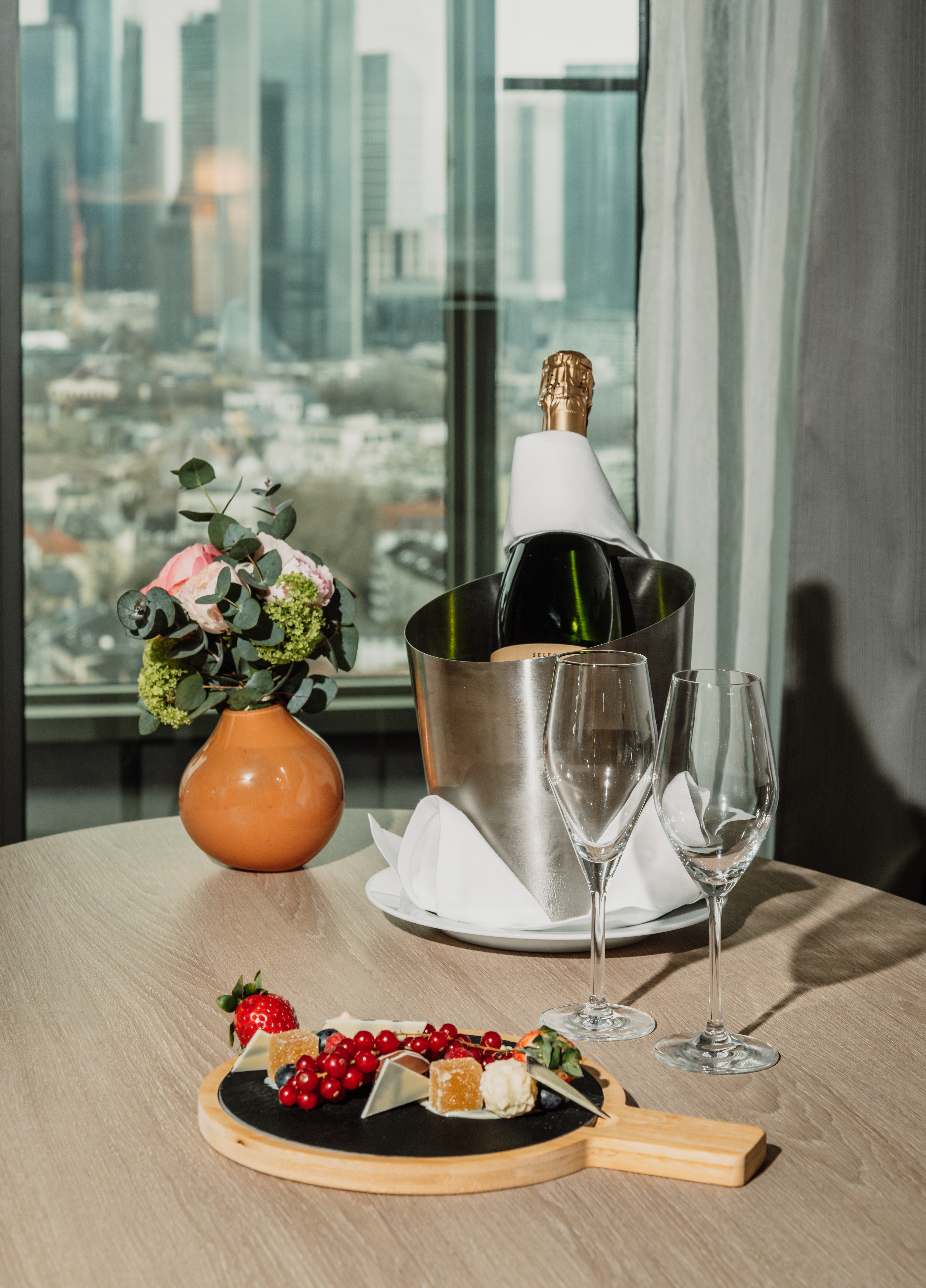 a bottle of champagne in a bucket next to a plate of fruit and a vase of flowers