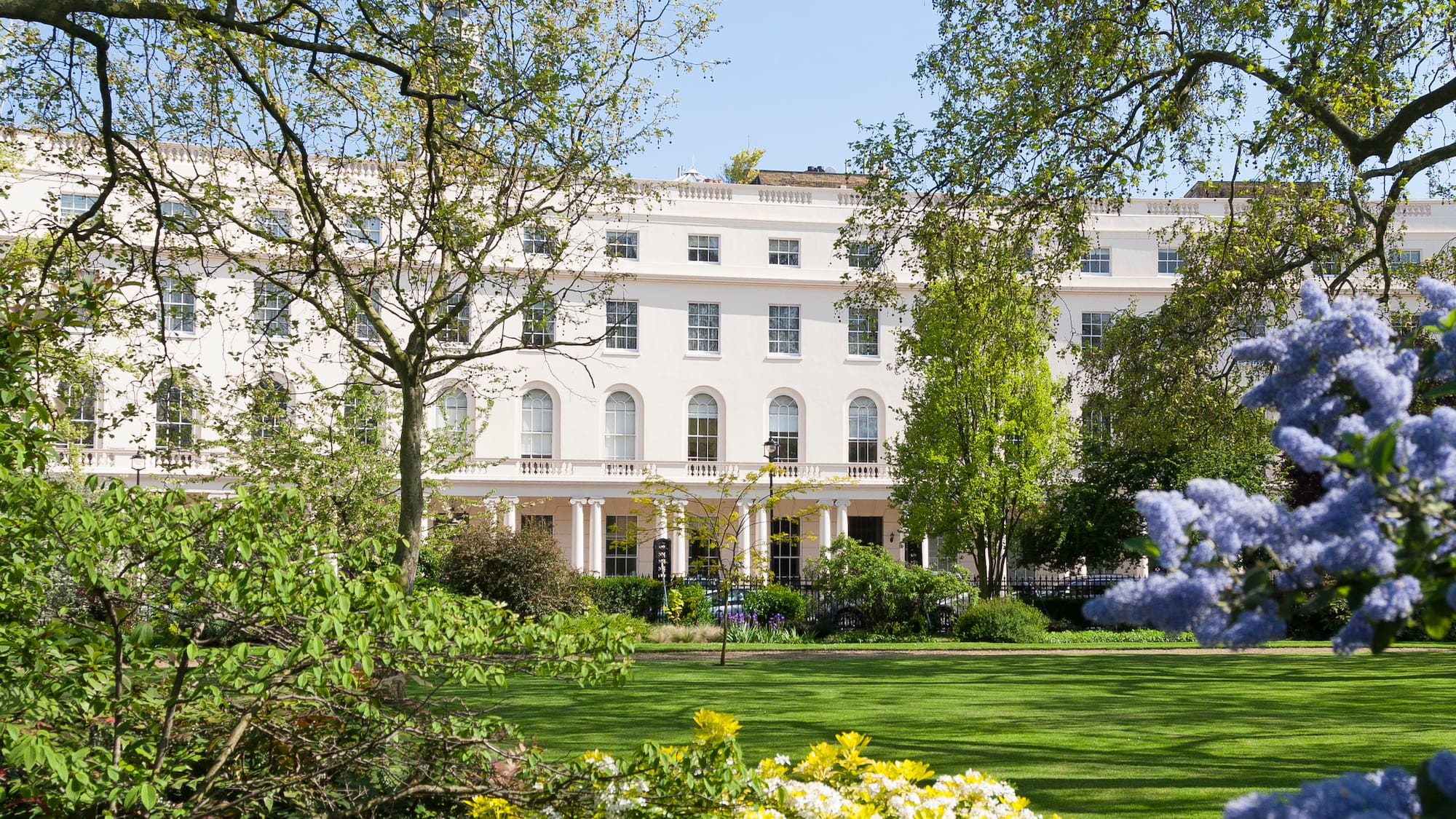 a white building with many windows and a lawn with trees and a blue sky