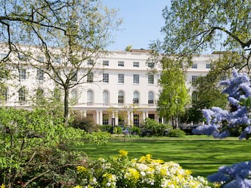 a white building with many windows and a lawn with trees and a blue sky