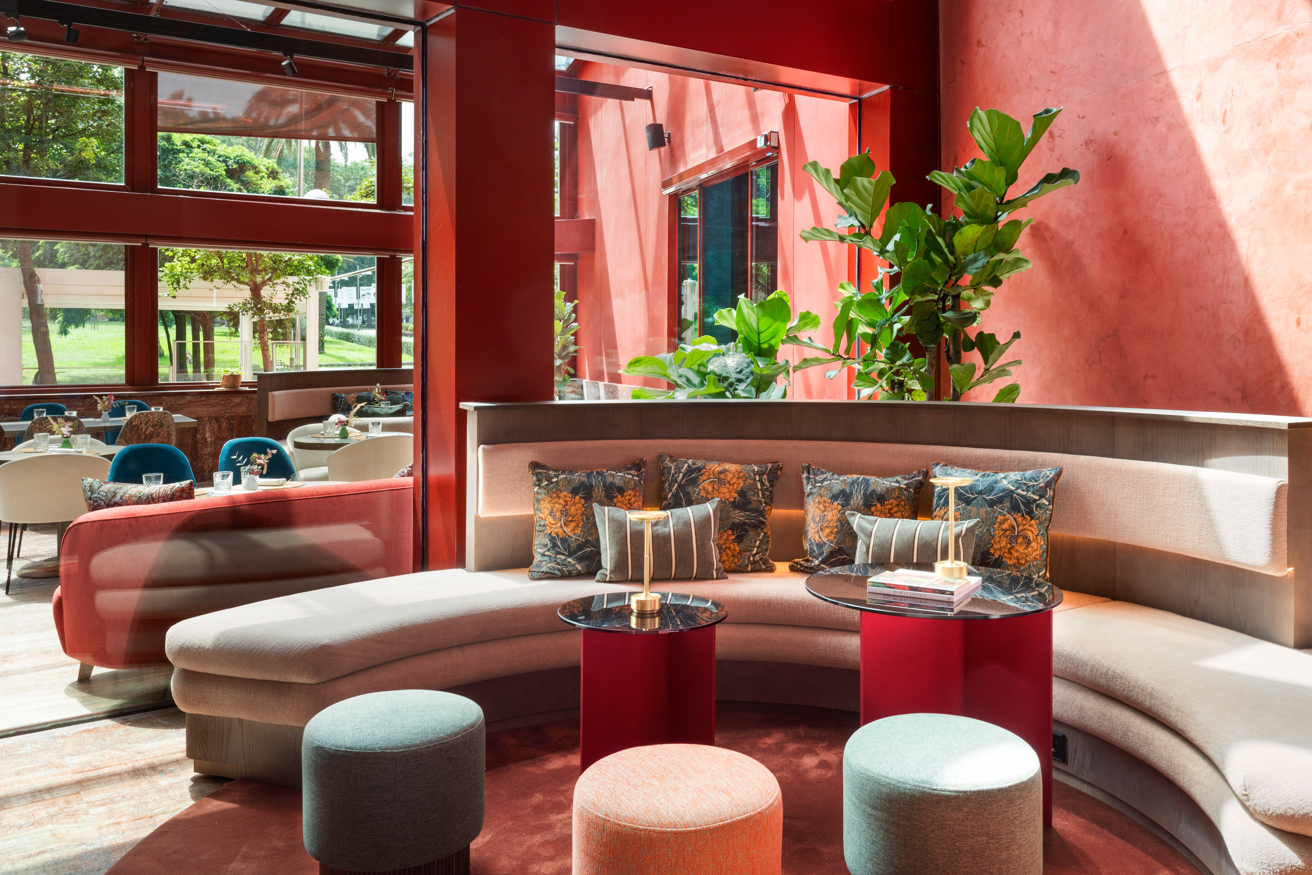 Modern red lounge design with curved sofa, lush plants, large windows.