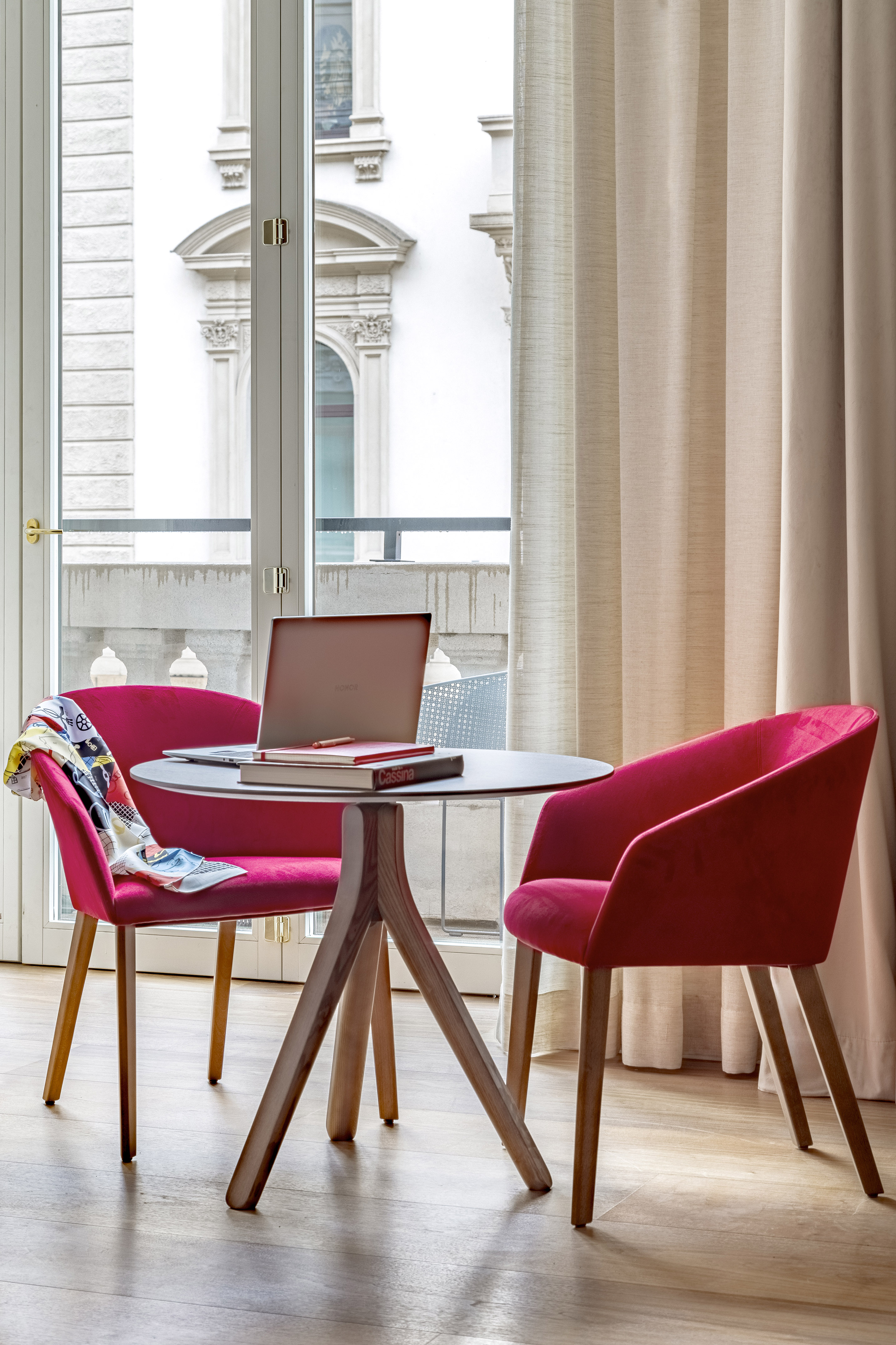 a table with a laptop and red chairs in a room with a balcony