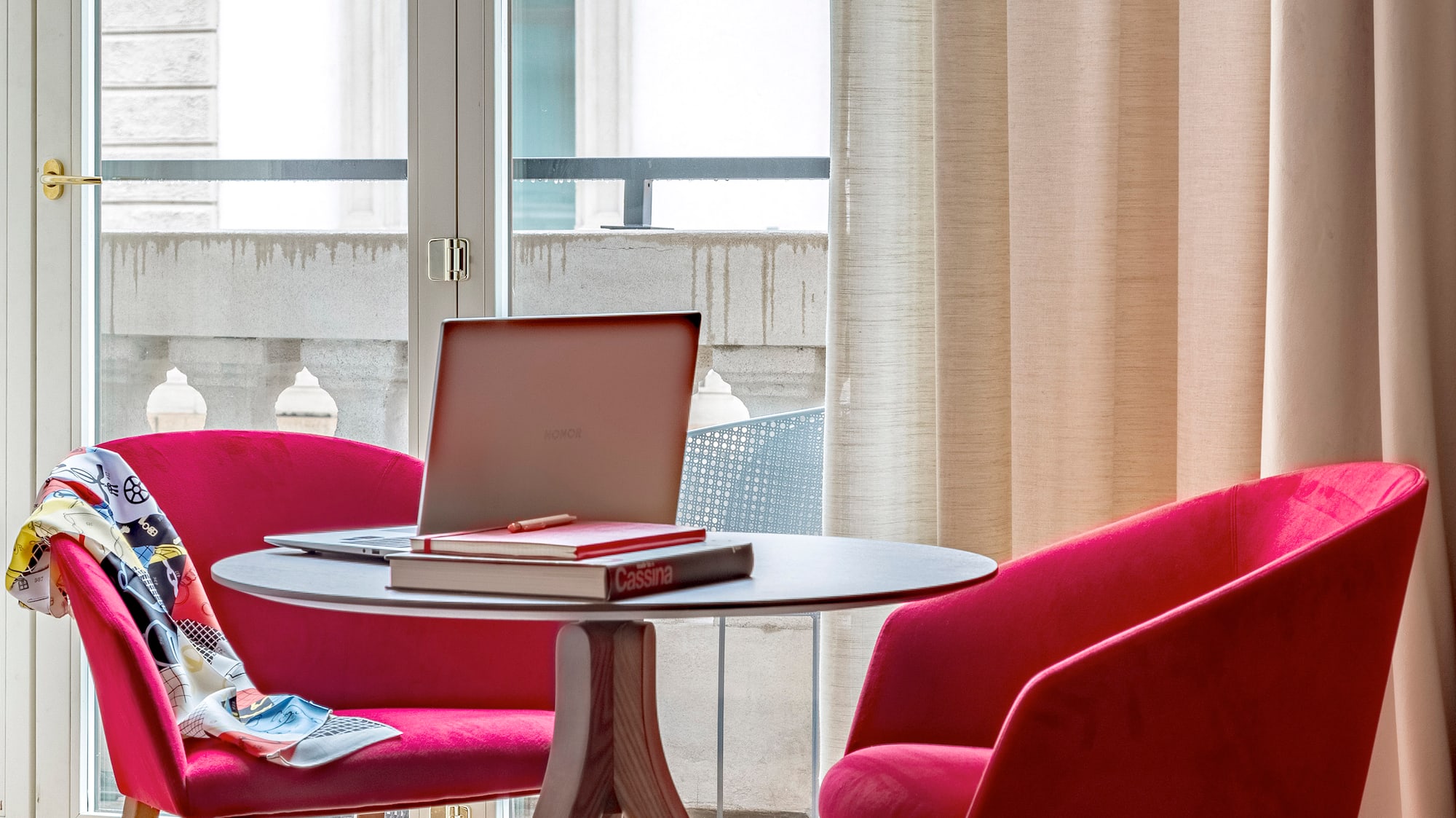 a table with a laptop and red chairs in a room with a balcony