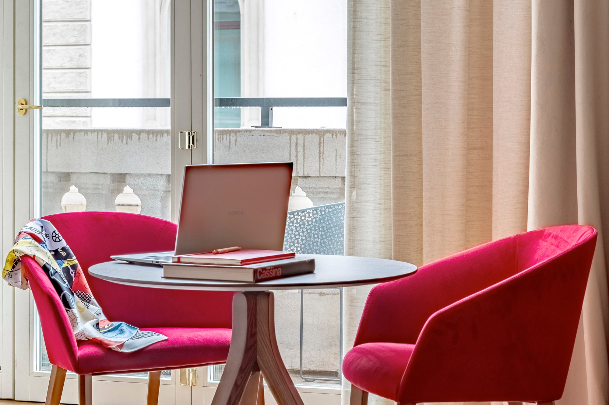 a table with a laptop and red chairs in a room with a balcony