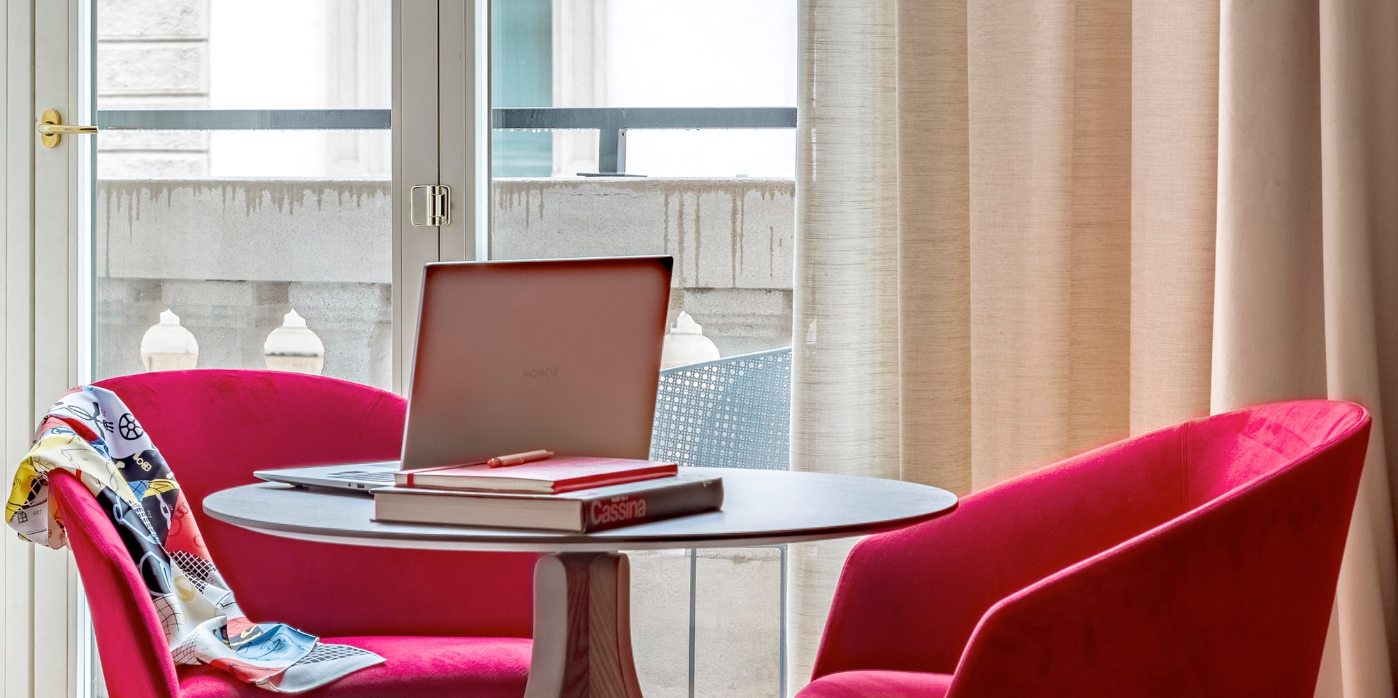 a table with a laptop and red chairs in a room with a balcony