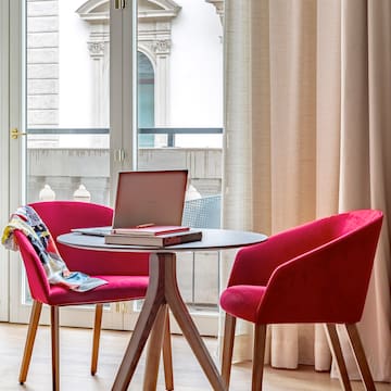 a table with a laptop and red chairs in a room with a balcony
