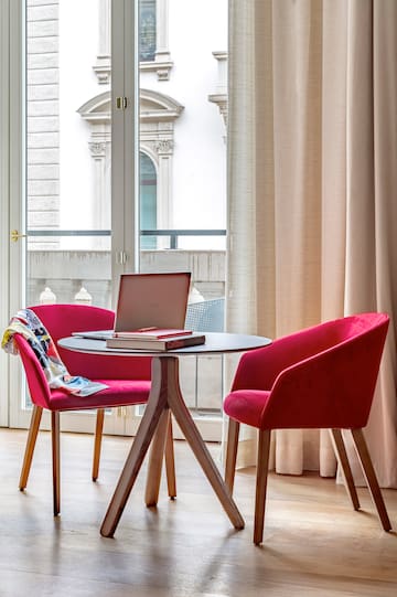 a table with a laptop and red chairs in a room with a balcony