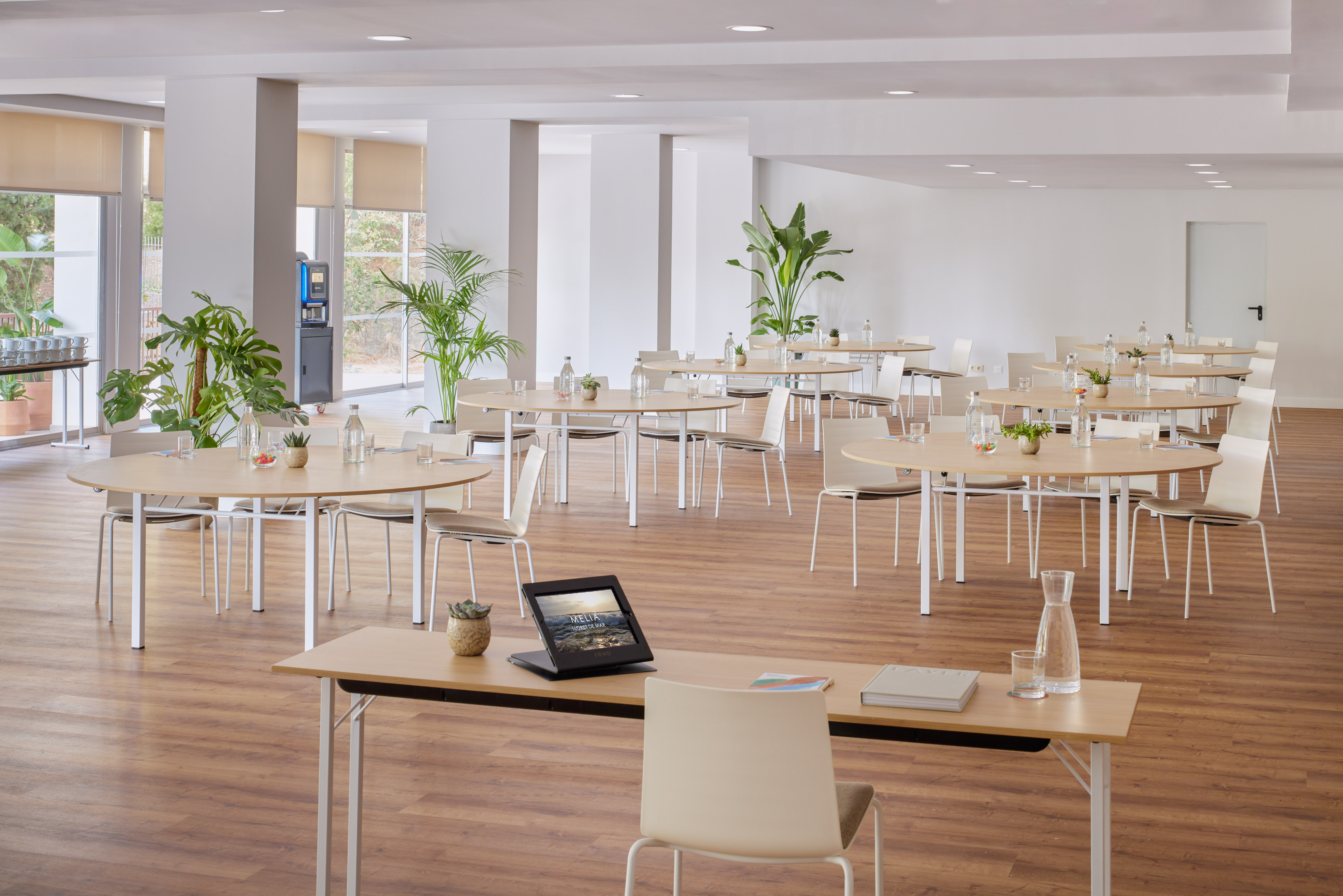 Modern conference room with round tables, chairs, plants, and natural light.