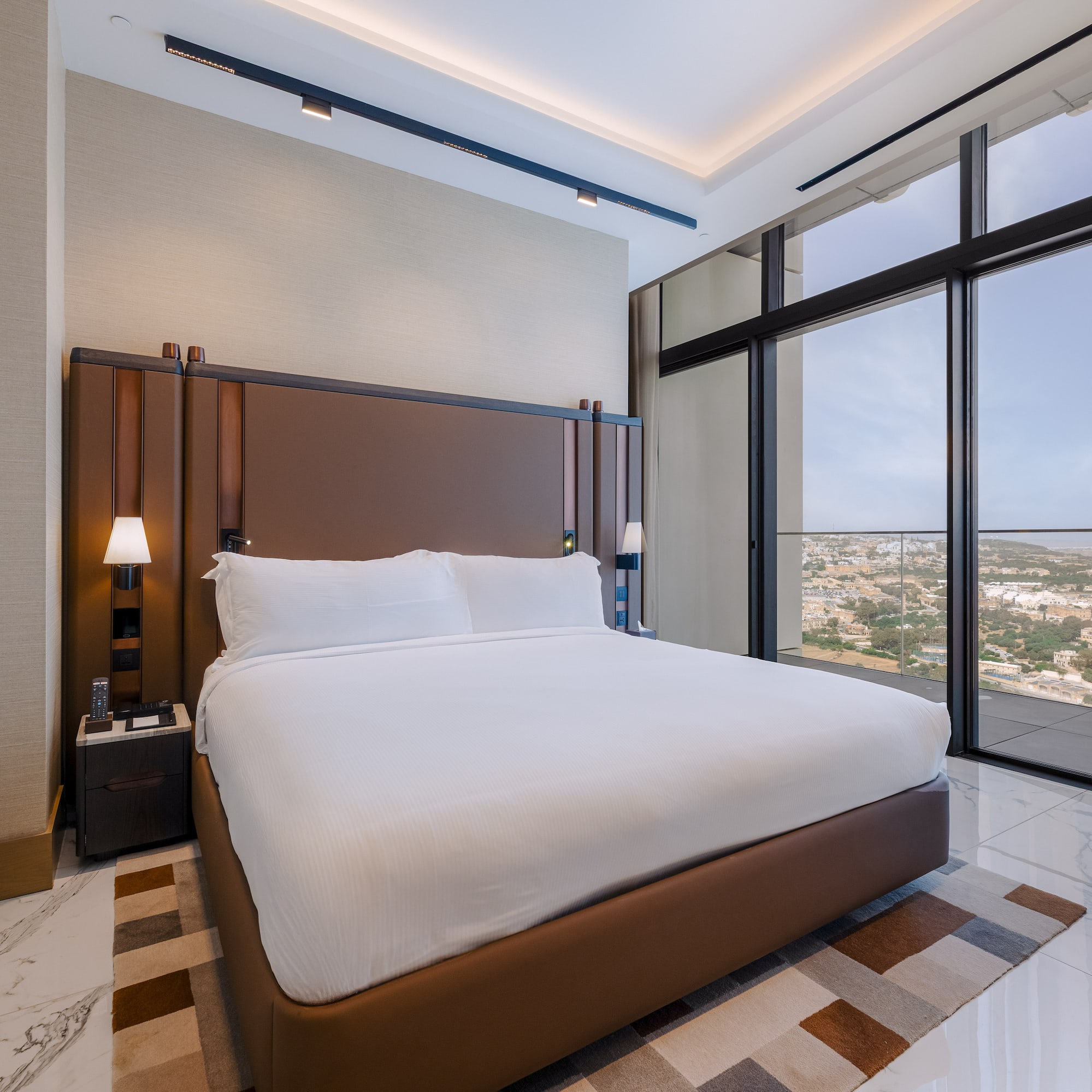 Elegant hotel room with king bed, brown headboard, and panoramic city views.
