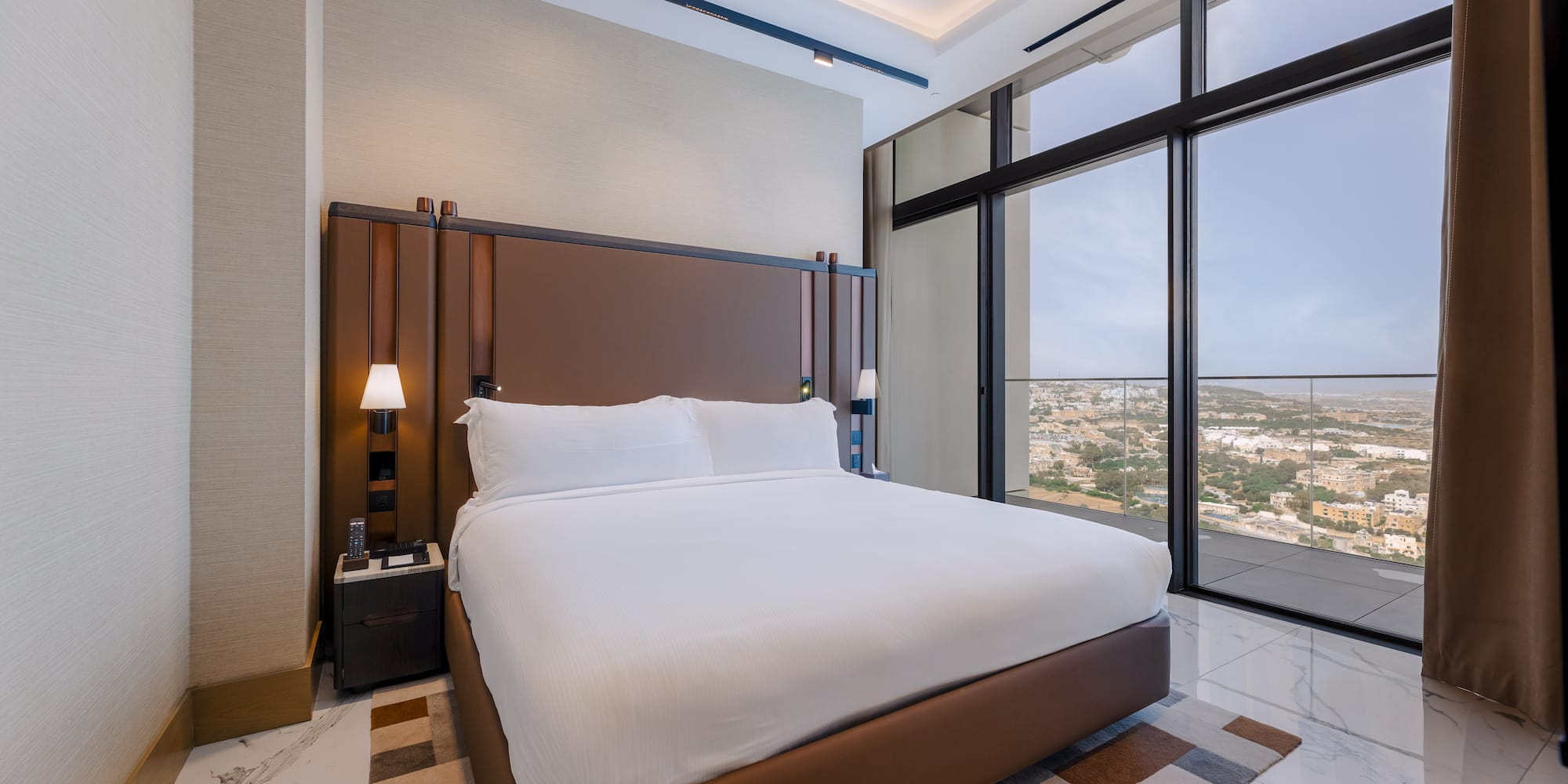 Elegant hotel room with king bed, brown headboard, and panoramic city views.
