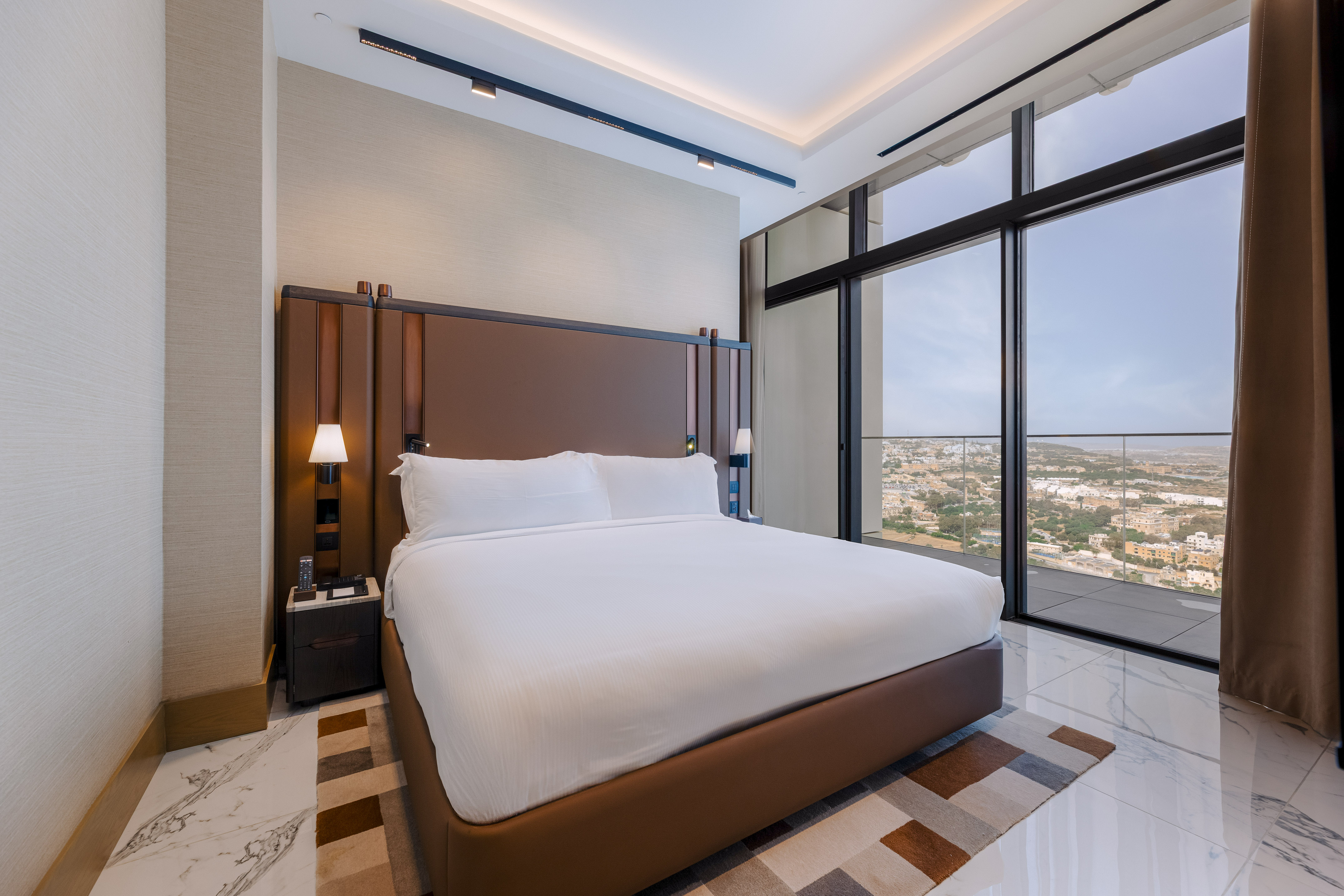Elegant hotel room with king bed, brown headboard, and panoramic city views.