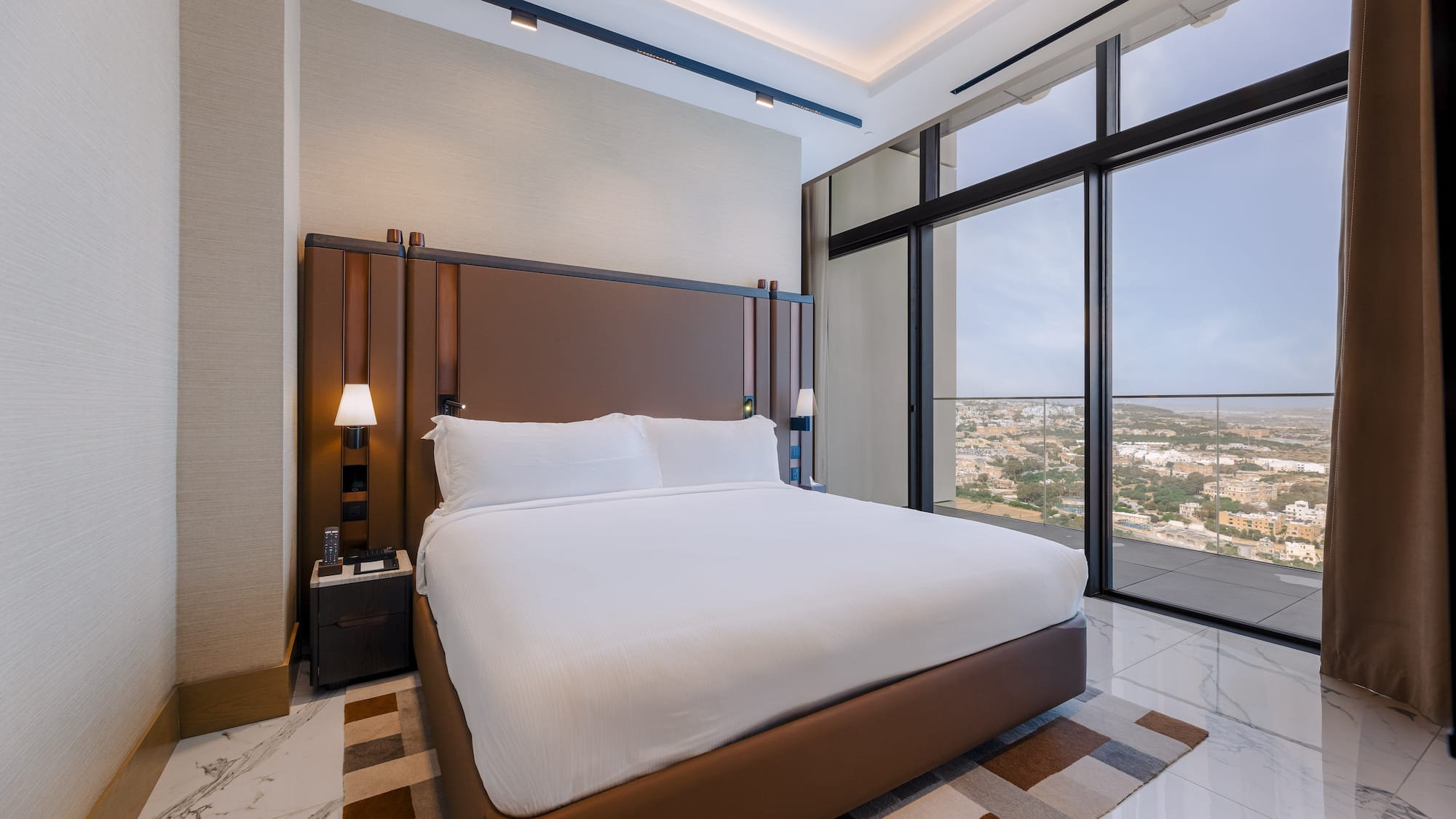 Elegant hotel room with king bed, brown headboard, and panoramic city views.