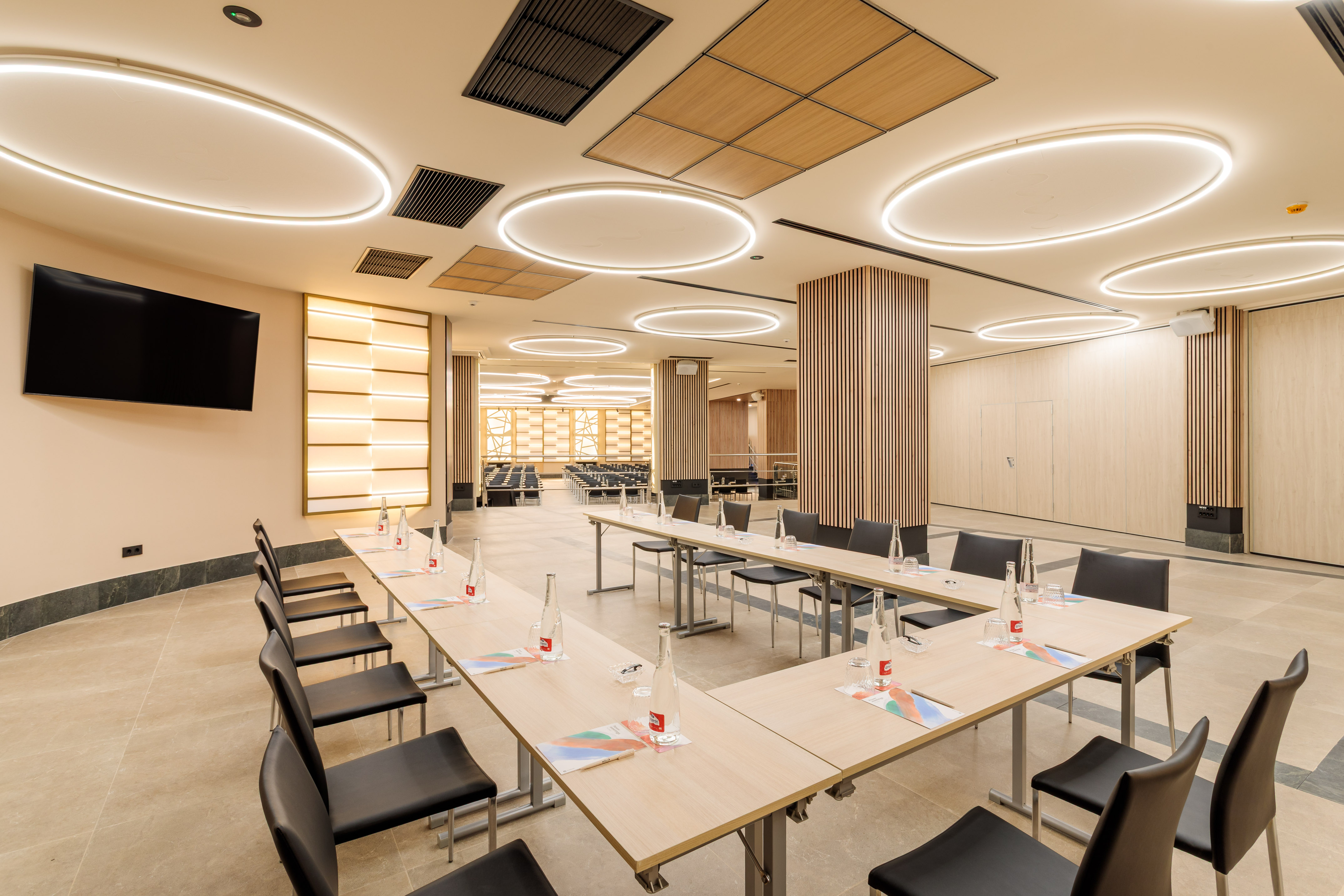 Modern hotel meeting room with U-shaped tables, black chairs, and ambient lighting.