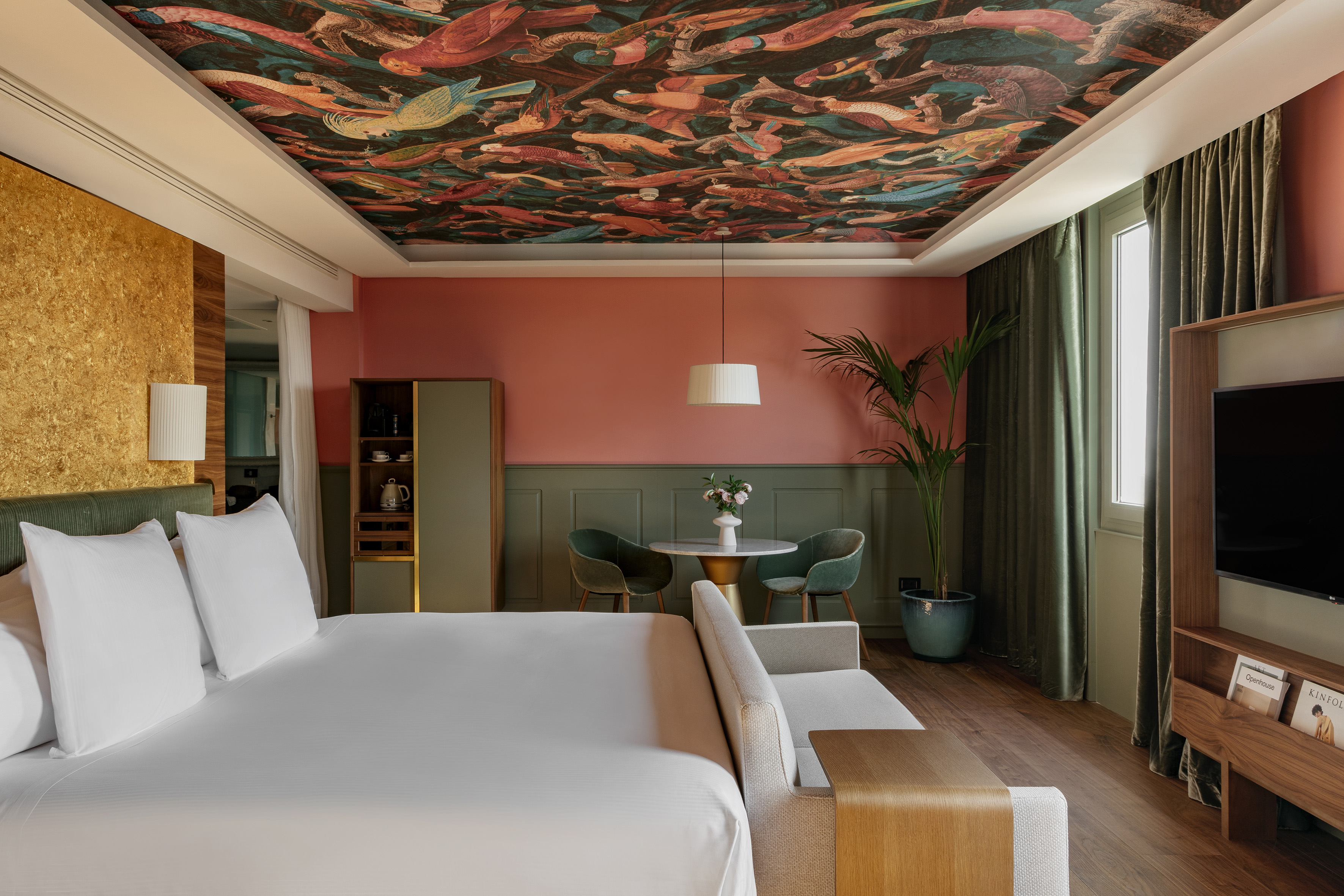 Unique hotel bedroom with vibrant bird-patterned ceiling and coral-green walls.