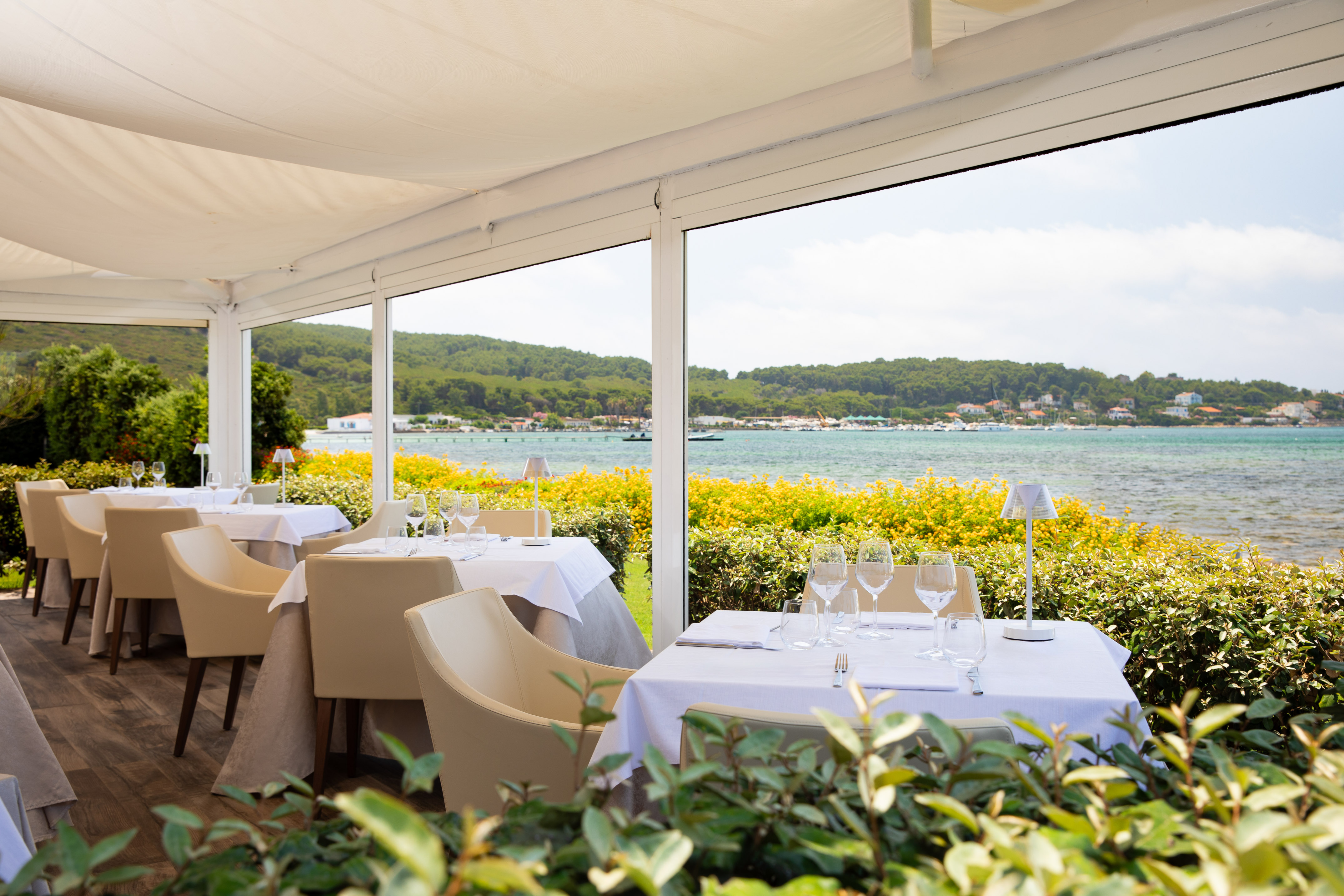 Outdoor dining with ocean view, set tables, and green hills.