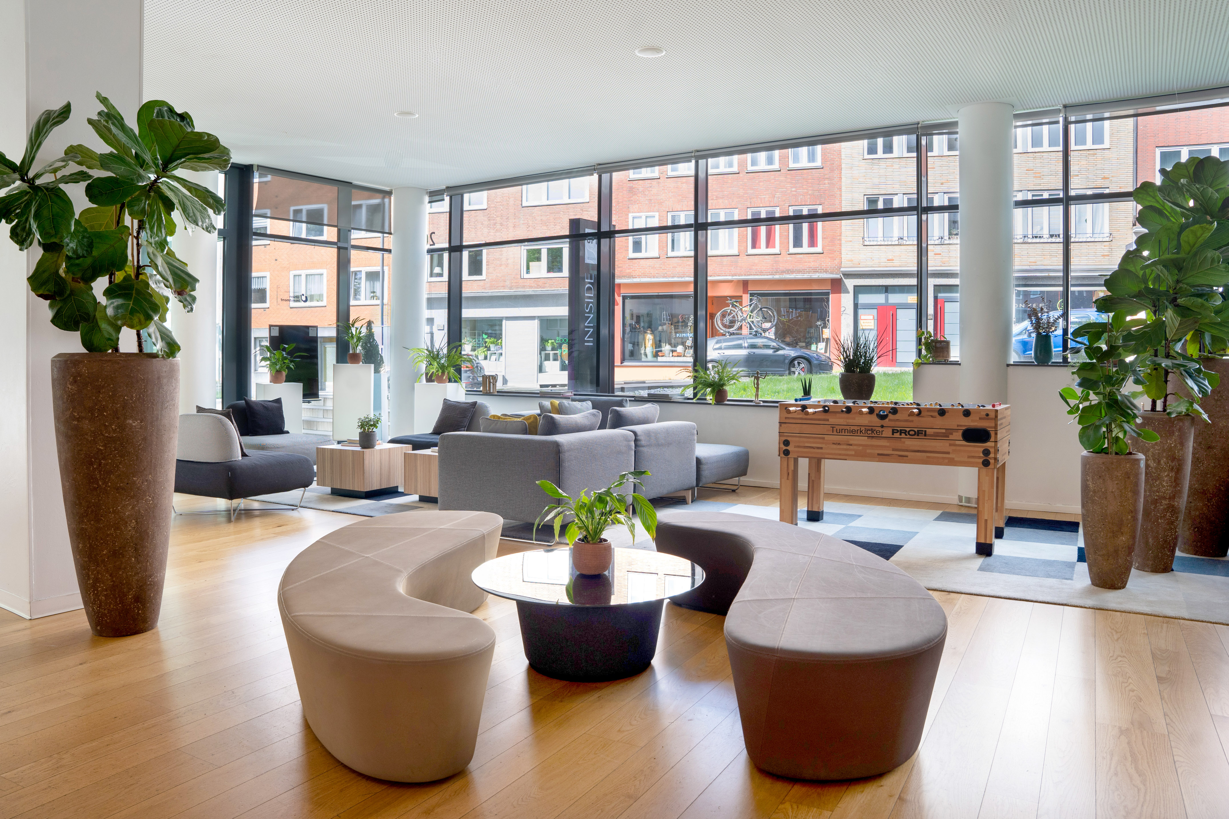 Modern lounge with gray sofas, foosball table, plants, and large windows.