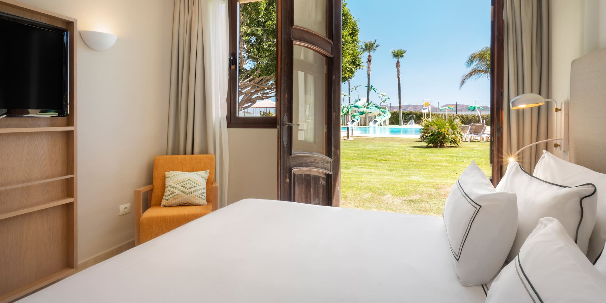a bed with white sheets and pillows in a room with a pool outside