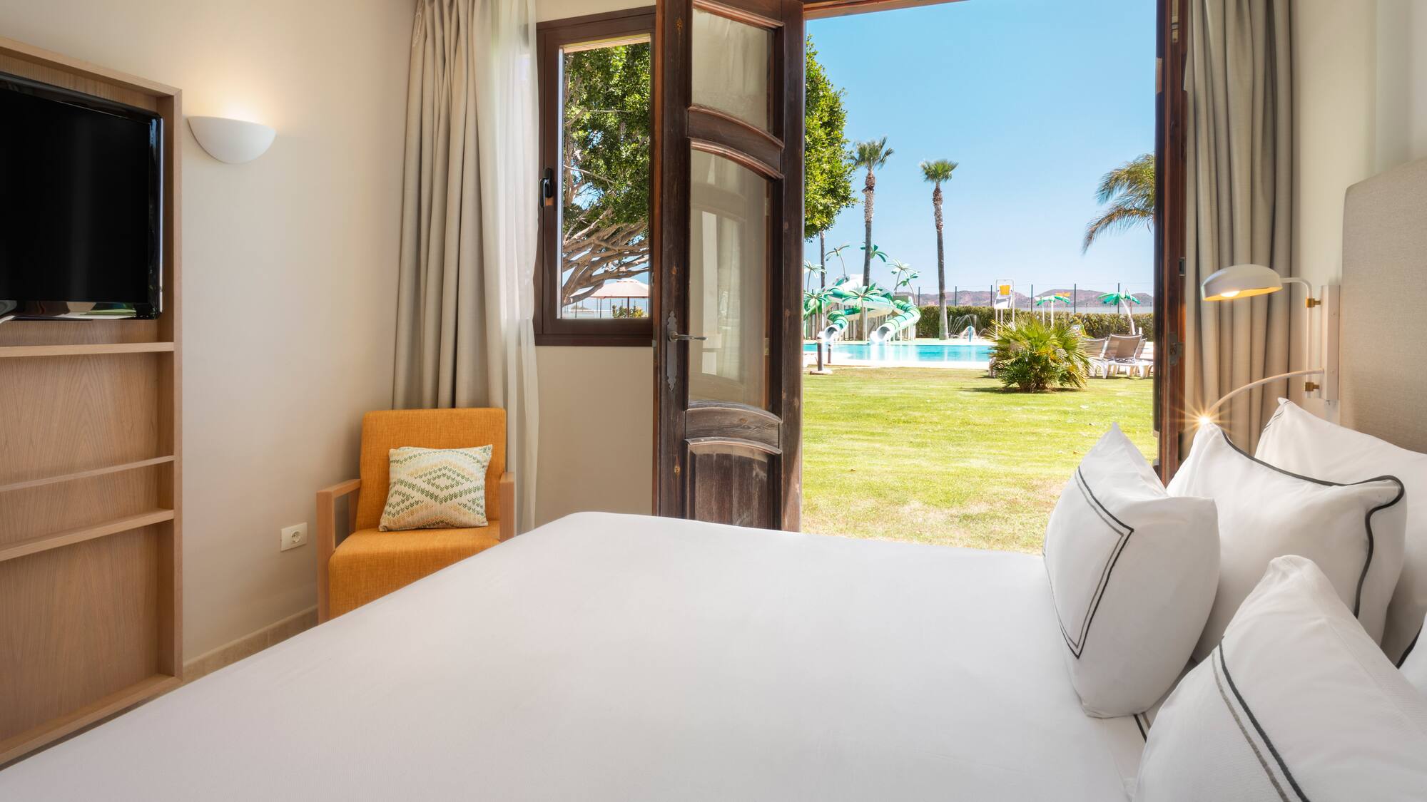 a bed with white sheets and pillows in a room with a pool outside