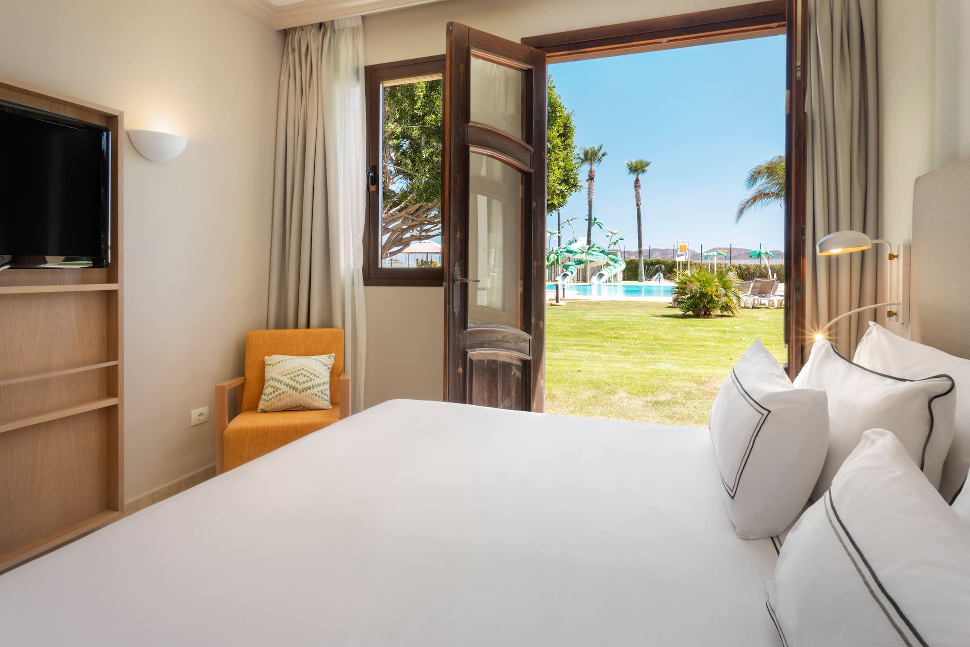 a bed with white sheets and pillows in a room with a pool outside