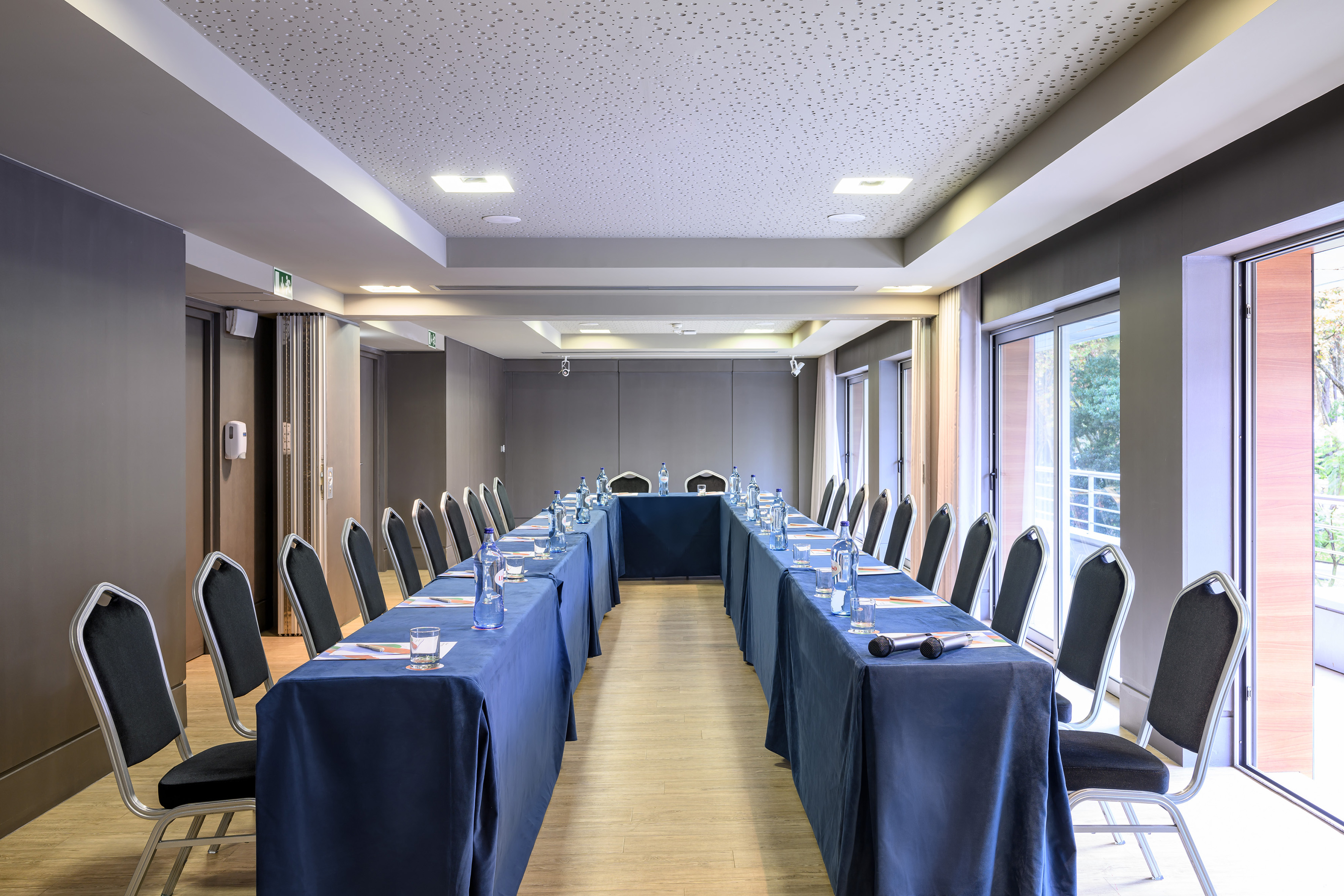 U-shaped conference room with blue tables, chairs, water, and bright windows.