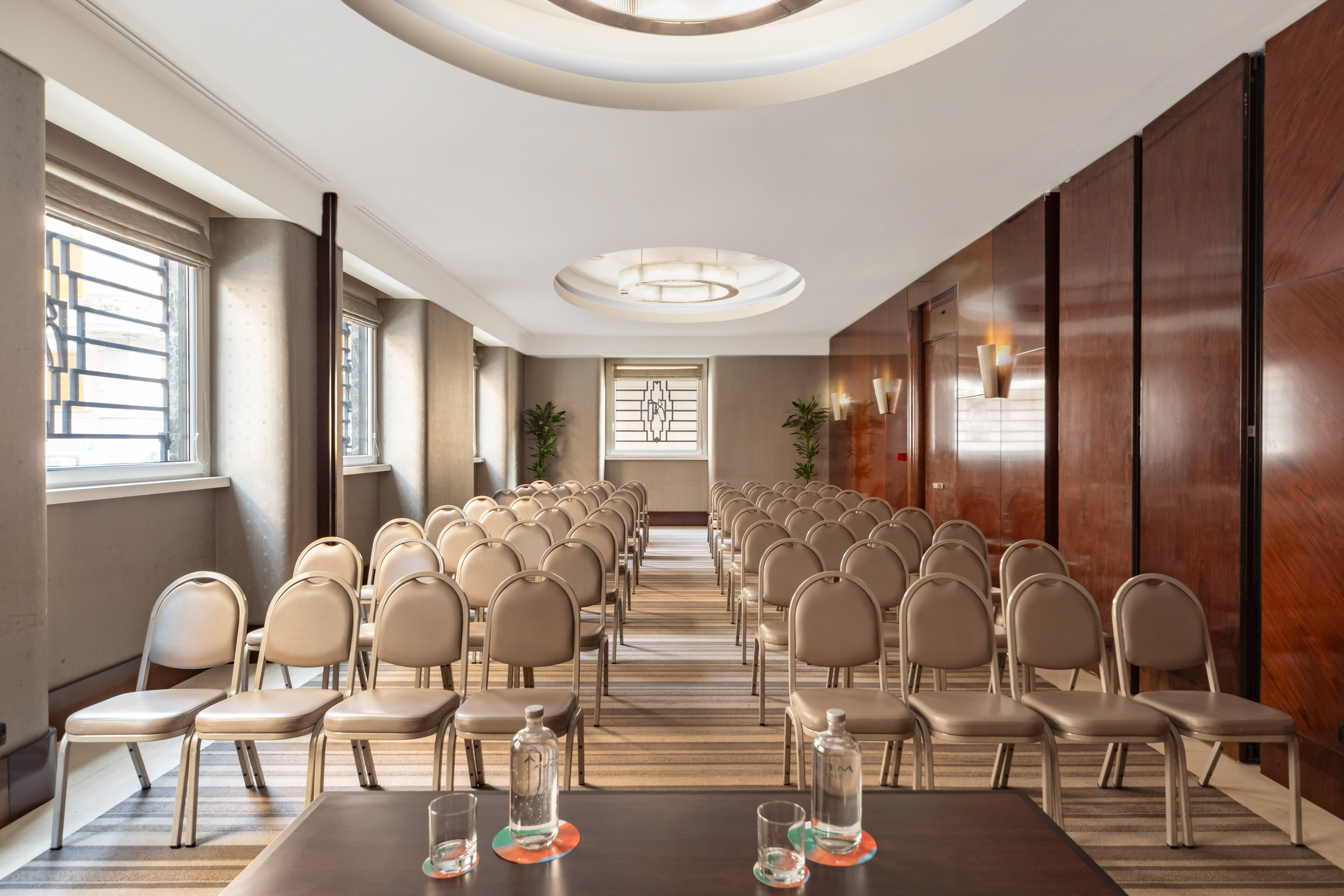Conference room with rows of beige chairs, patterned carpet, and wooden walls.