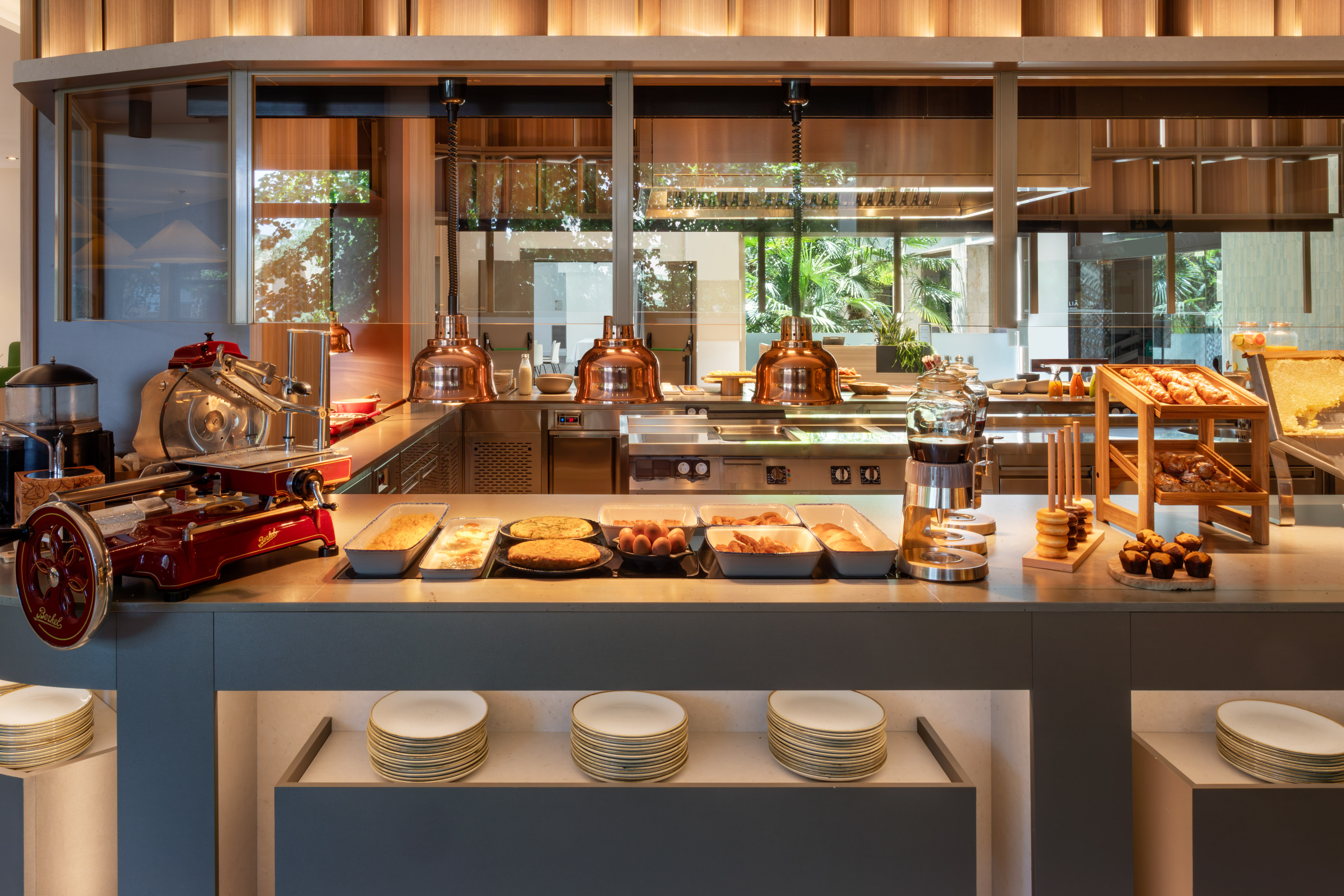 Modern hotel breakfast buffet with pastries, eggs, hot food, and a slicer.