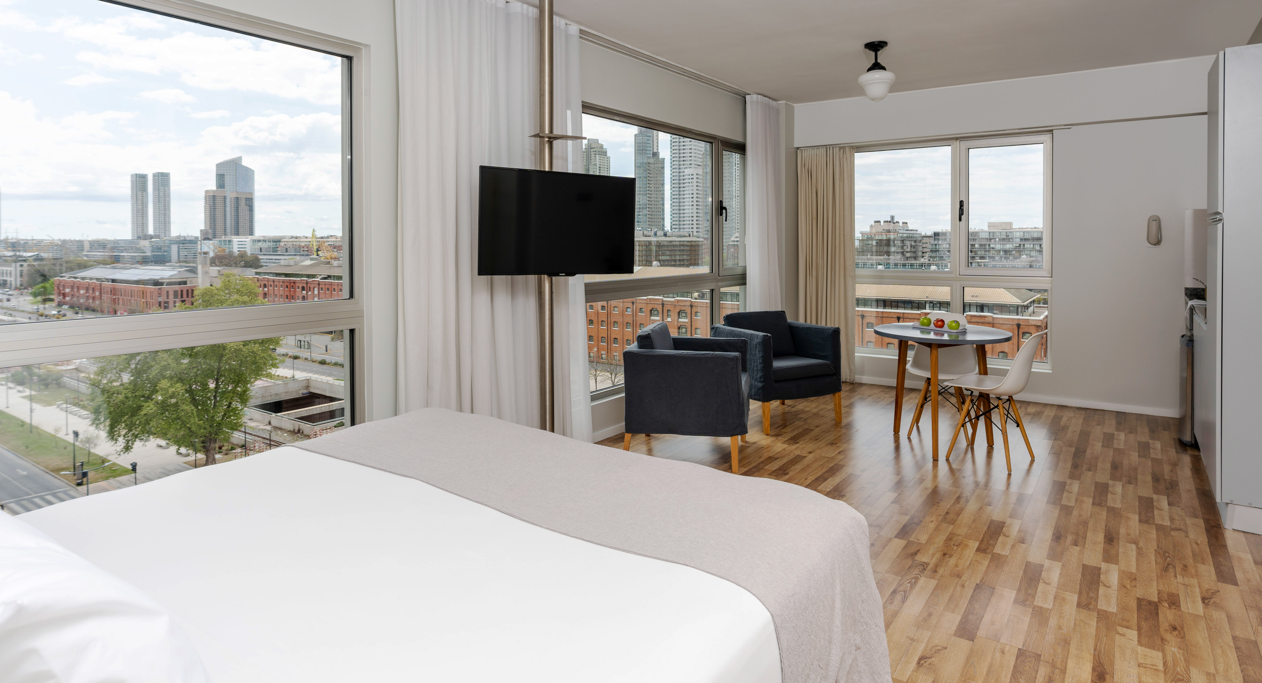 Modern studio apartment with city view, bed, dining table, and living area.
