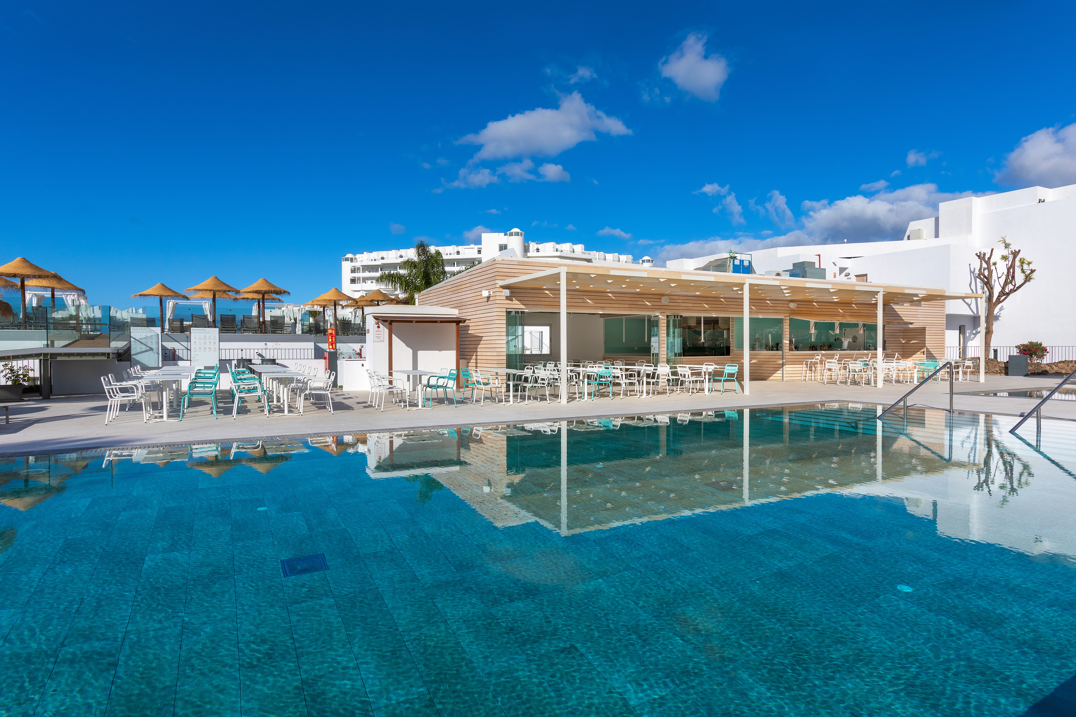 Sunny resort swimming pool with modern wooden poolside bar and outdoor seating.