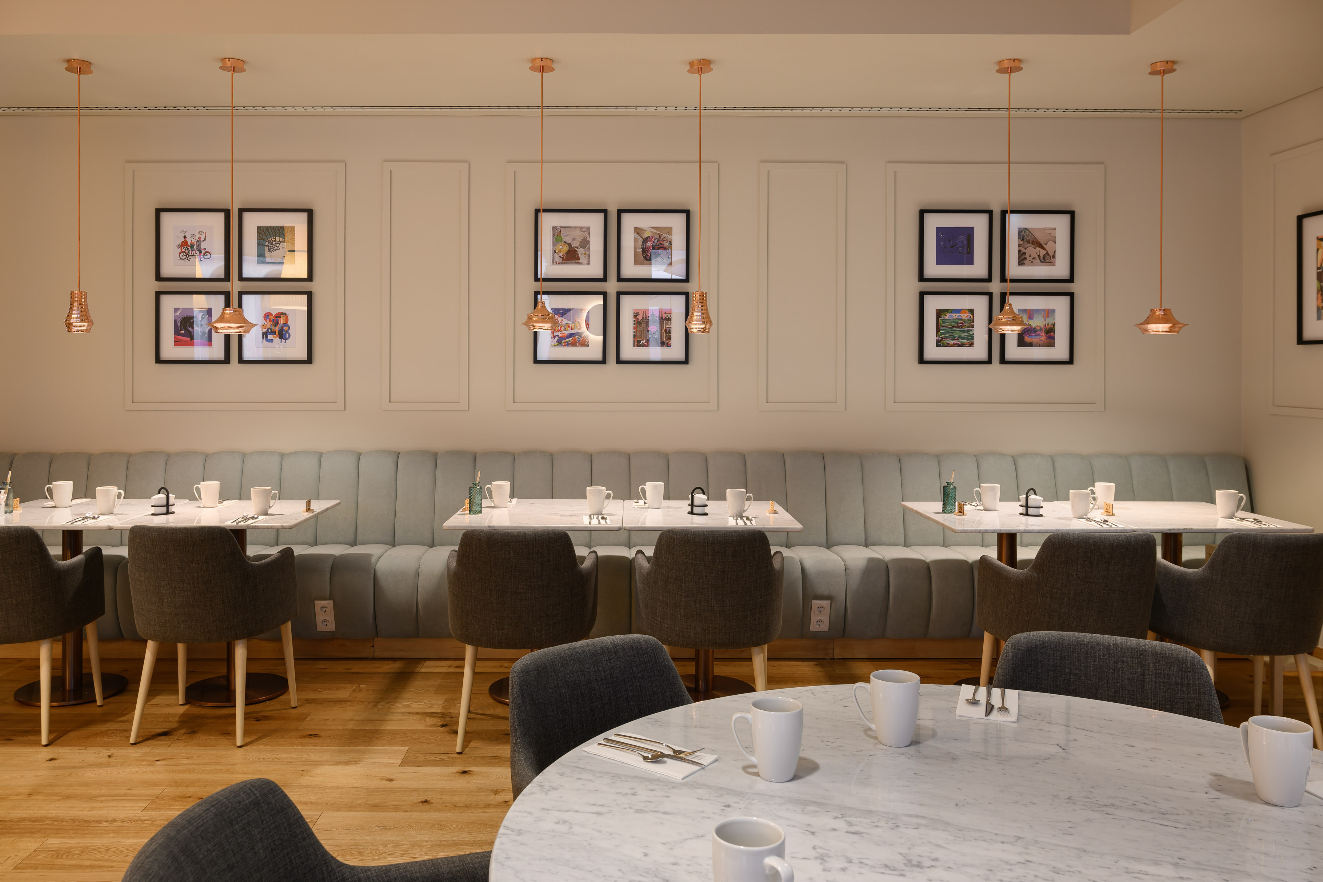 Modern restaurant interior with booth seating, marble tables, and copper pendant lights.