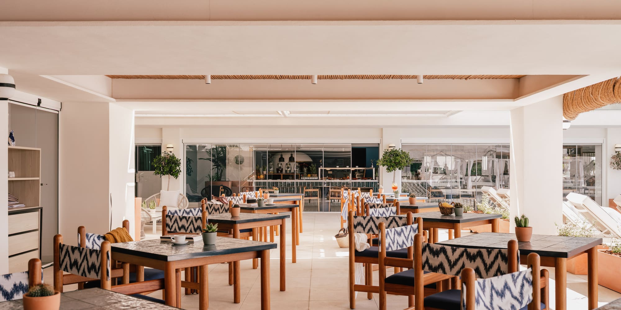 Bright outdoor restaurant, wooden tables, patterned chairs, bamboo ceiling.