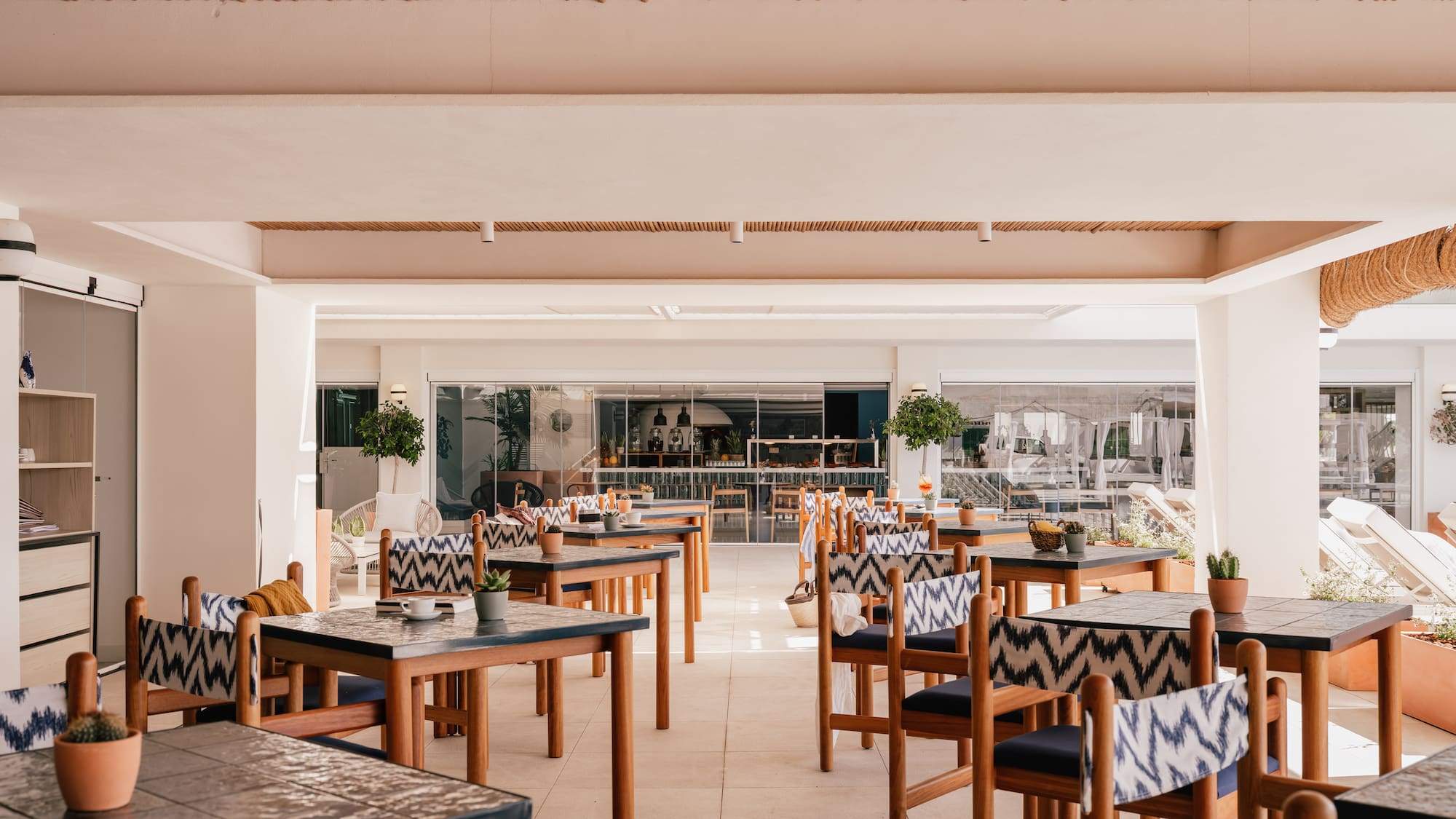 Bright outdoor restaurant, wooden tables, patterned chairs, bamboo ceiling.