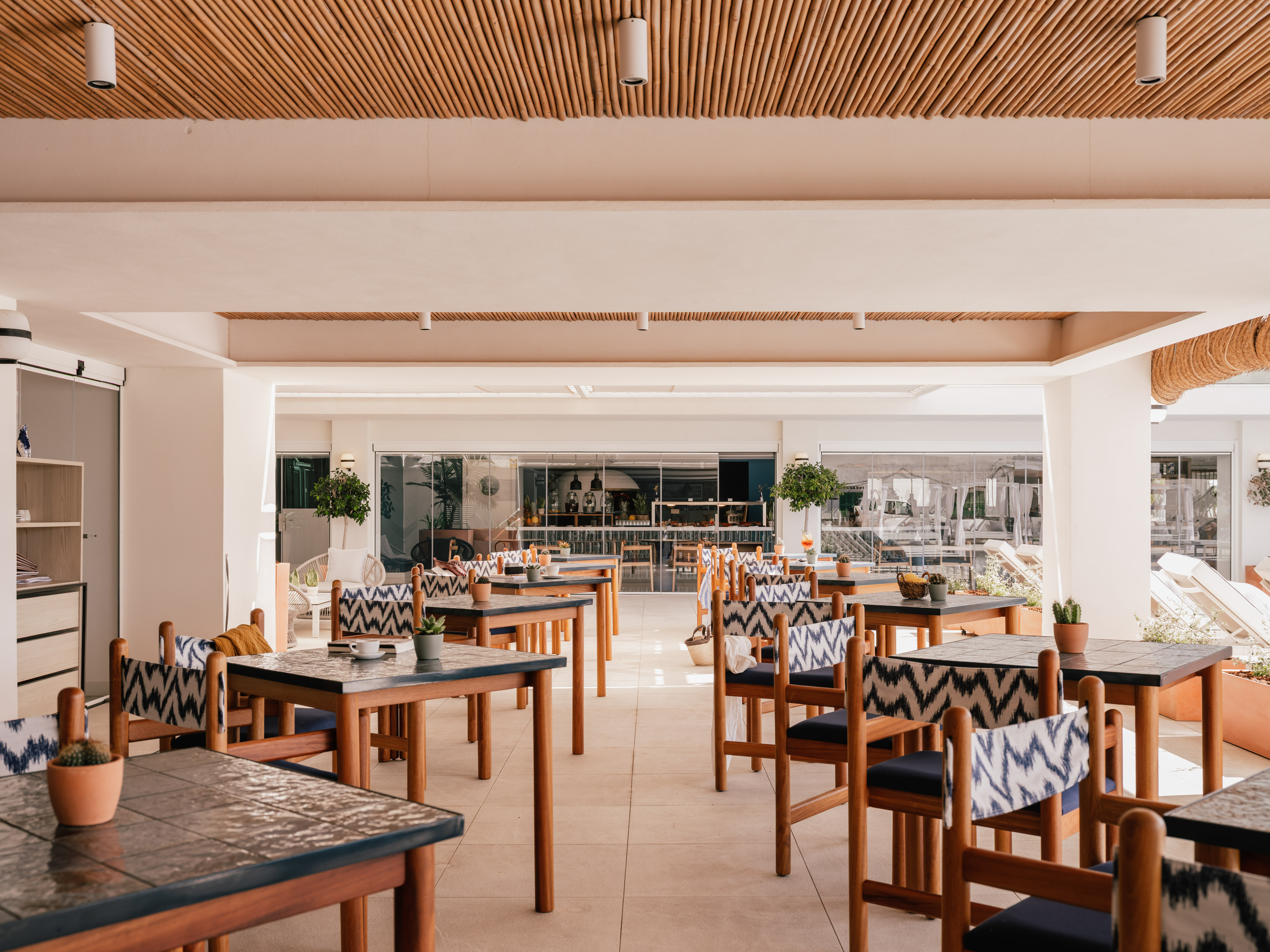 Bright outdoor restaurant, wooden tables, patterned chairs, bamboo ceiling.