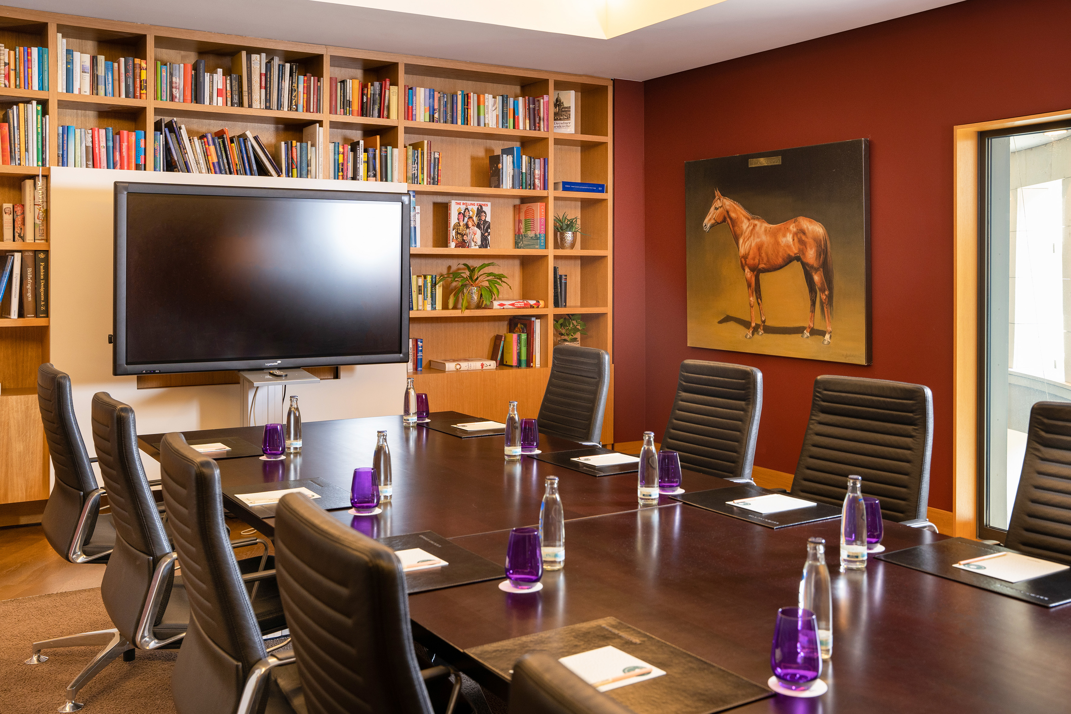 Boardroom with dark table, black leather chairs, large TV, and bookshelf wall. - CONLounge - Innside Dresda, Dresda