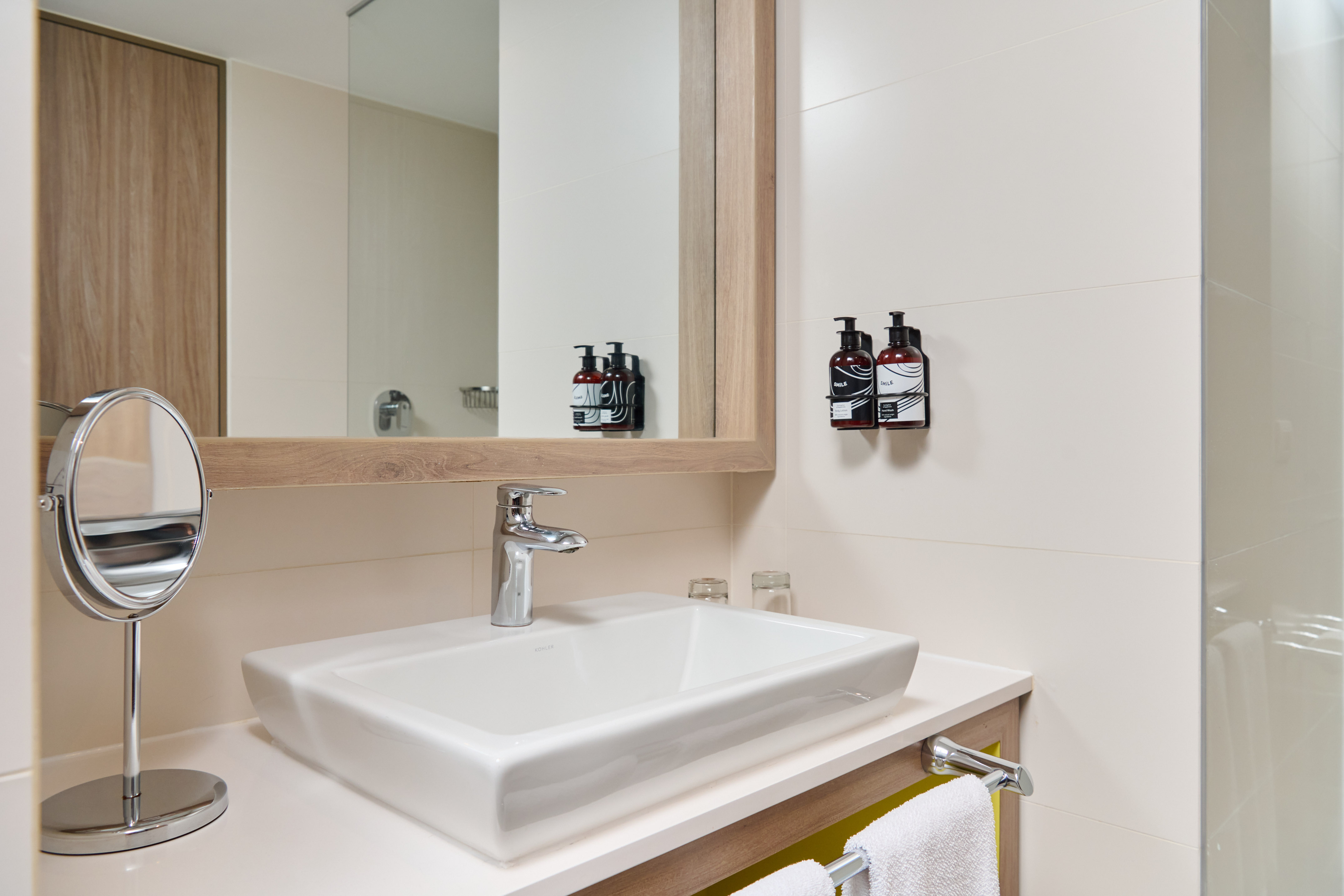 Modern hotel bathroom vanity with white sink, large mirror, and amenities.