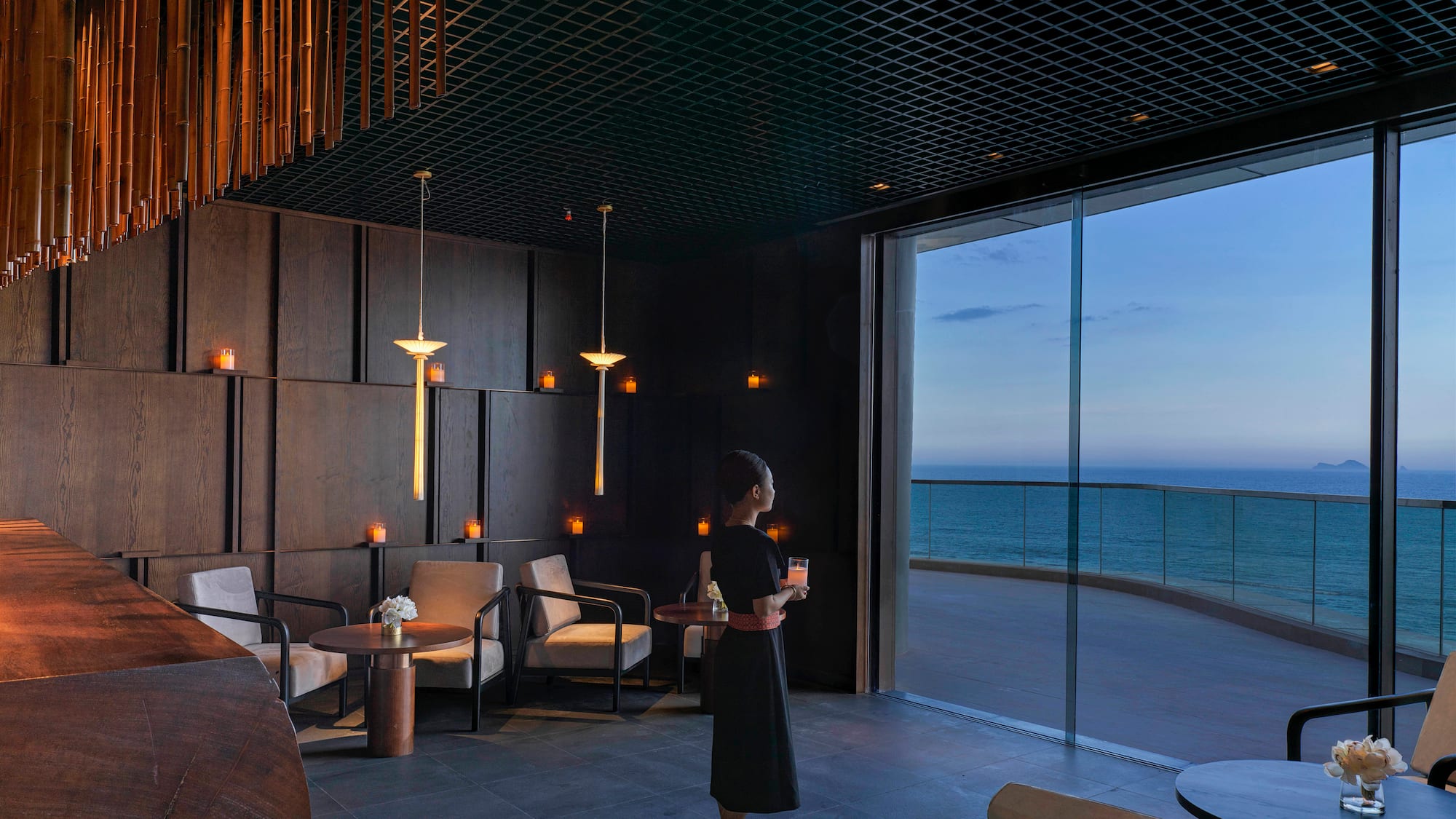 a woman holding a drink in a room with a large window overlooking the ocean