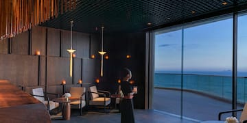 a woman holding a drink in a room with a large window overlooking the ocean