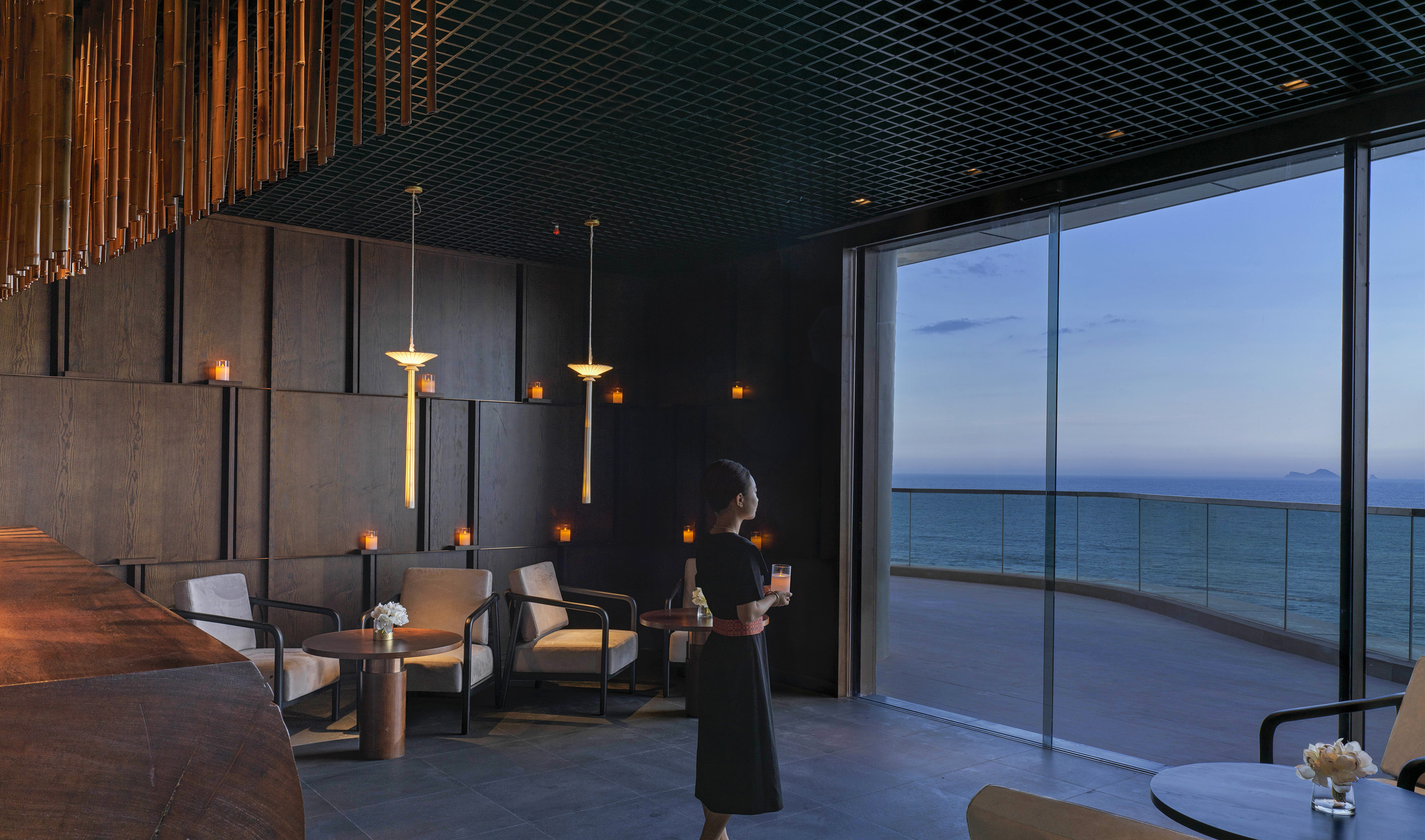 Woman in luxury bar, enjoying ocean view at dusk with a drink.