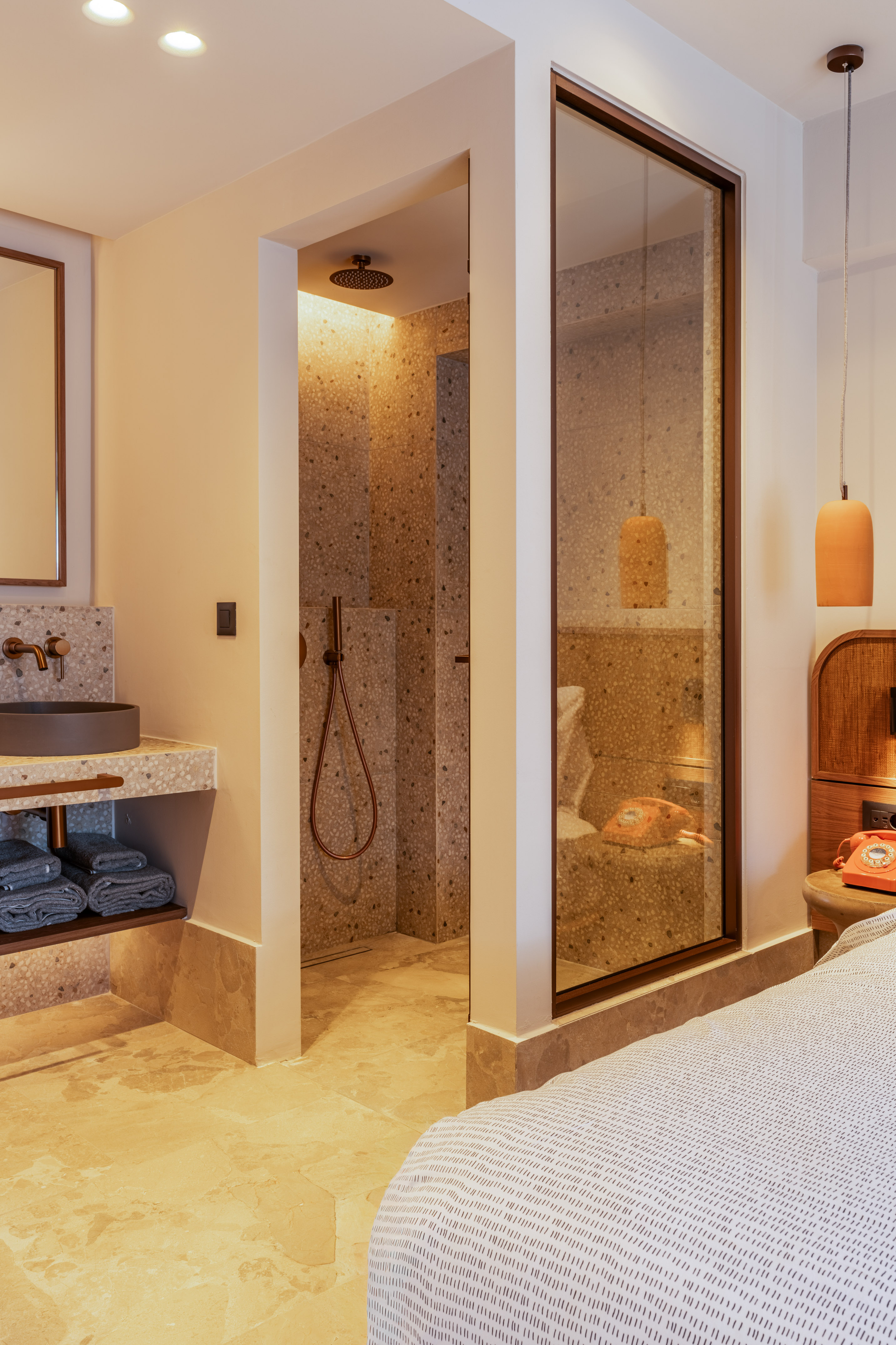 Modern hotel room with open-concept terrazzo bathroom and glass shower.