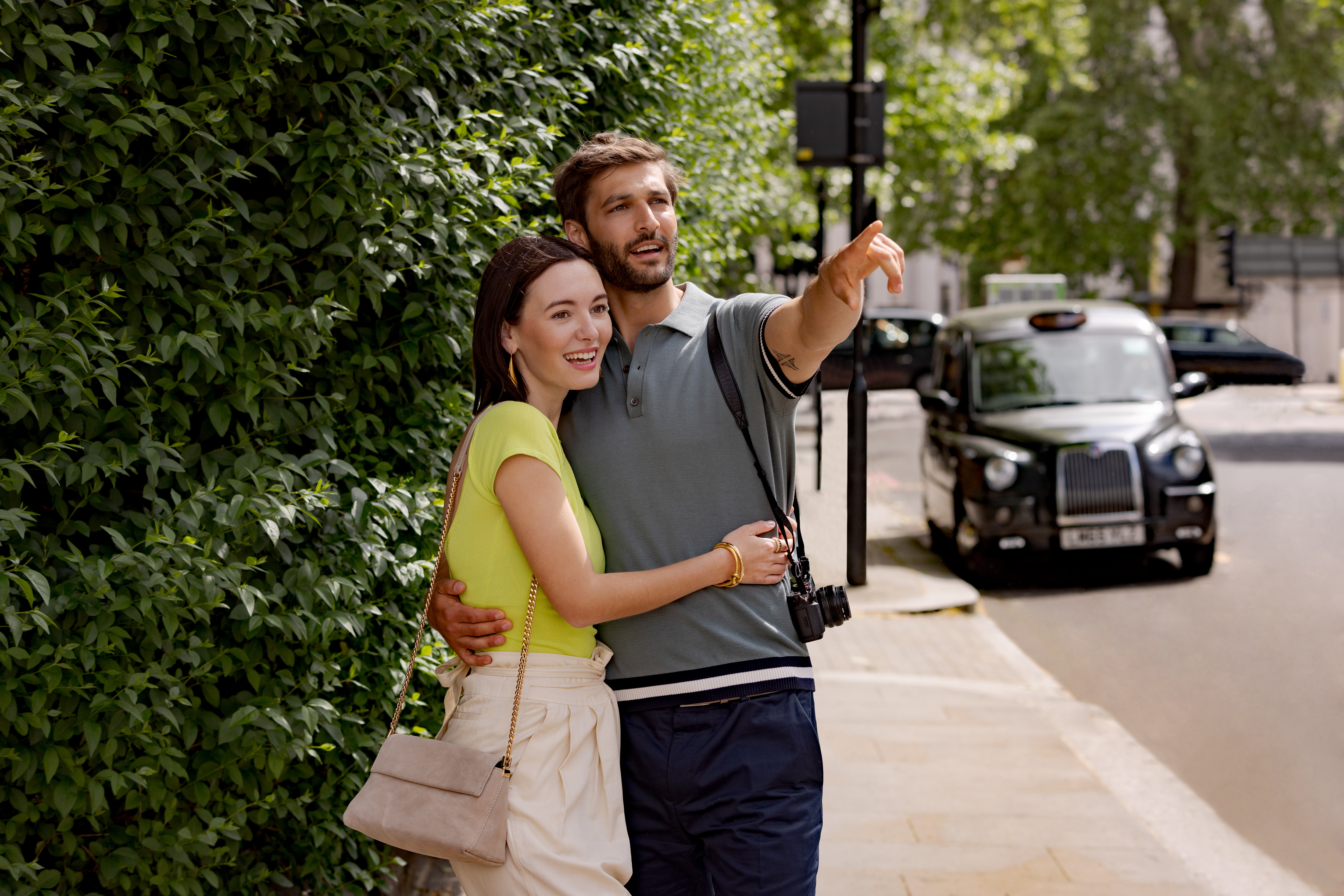 A man and a woman stand on the sidewalk, both pointing.